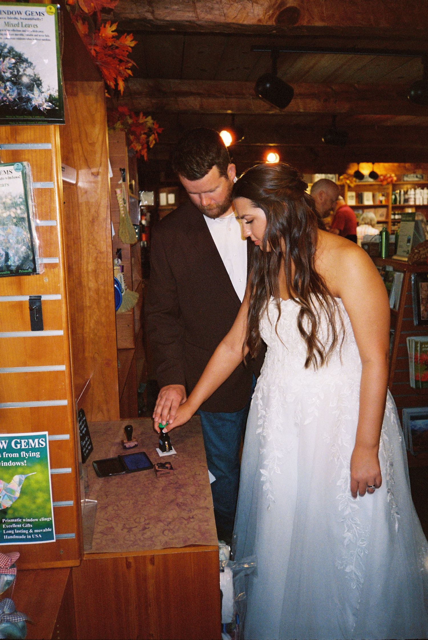 A couple in wedding attire looking down at something in a rustic indoor setting with autumn decorations.