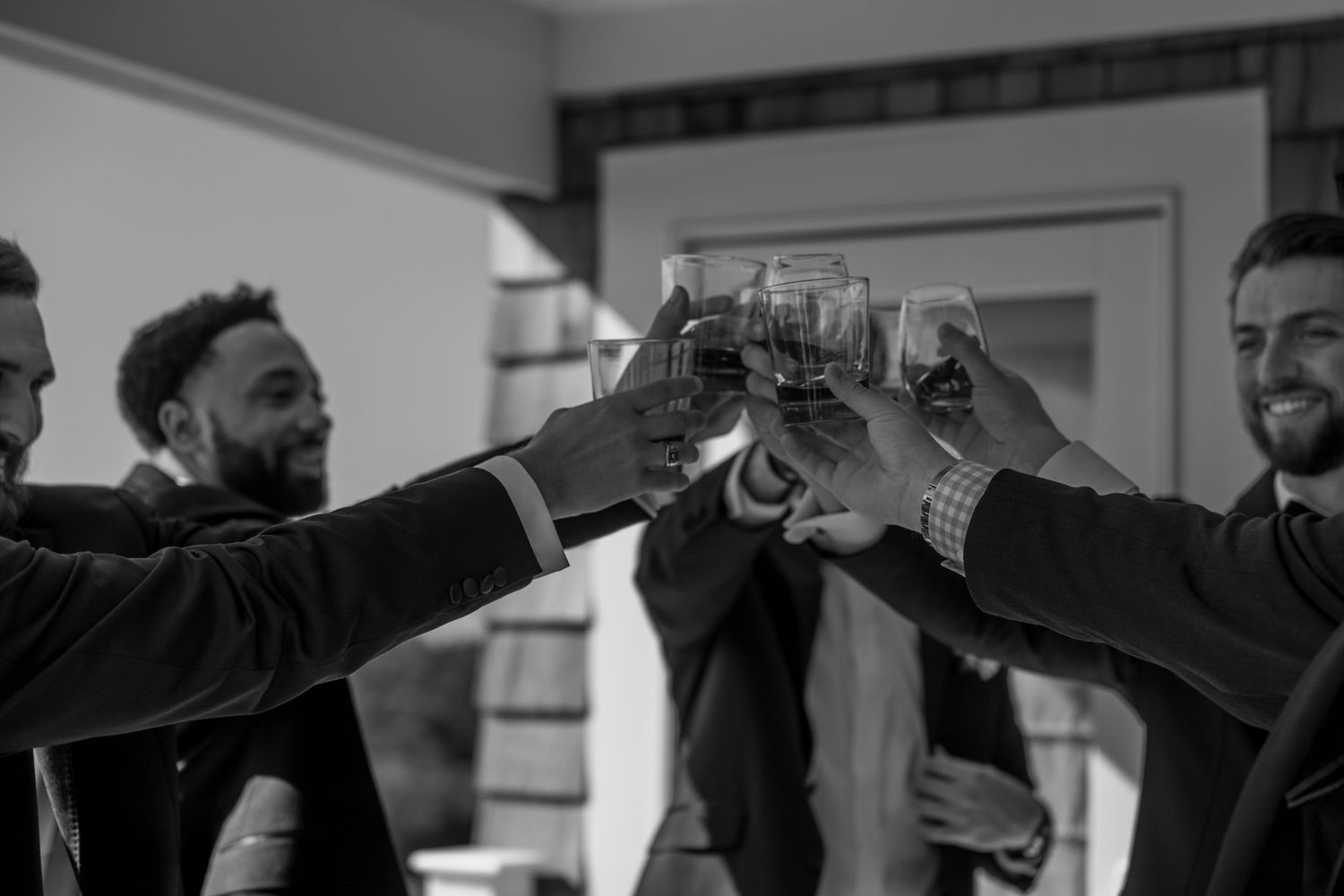 Black and white photo of groomsmen clinking glasses in celebration.