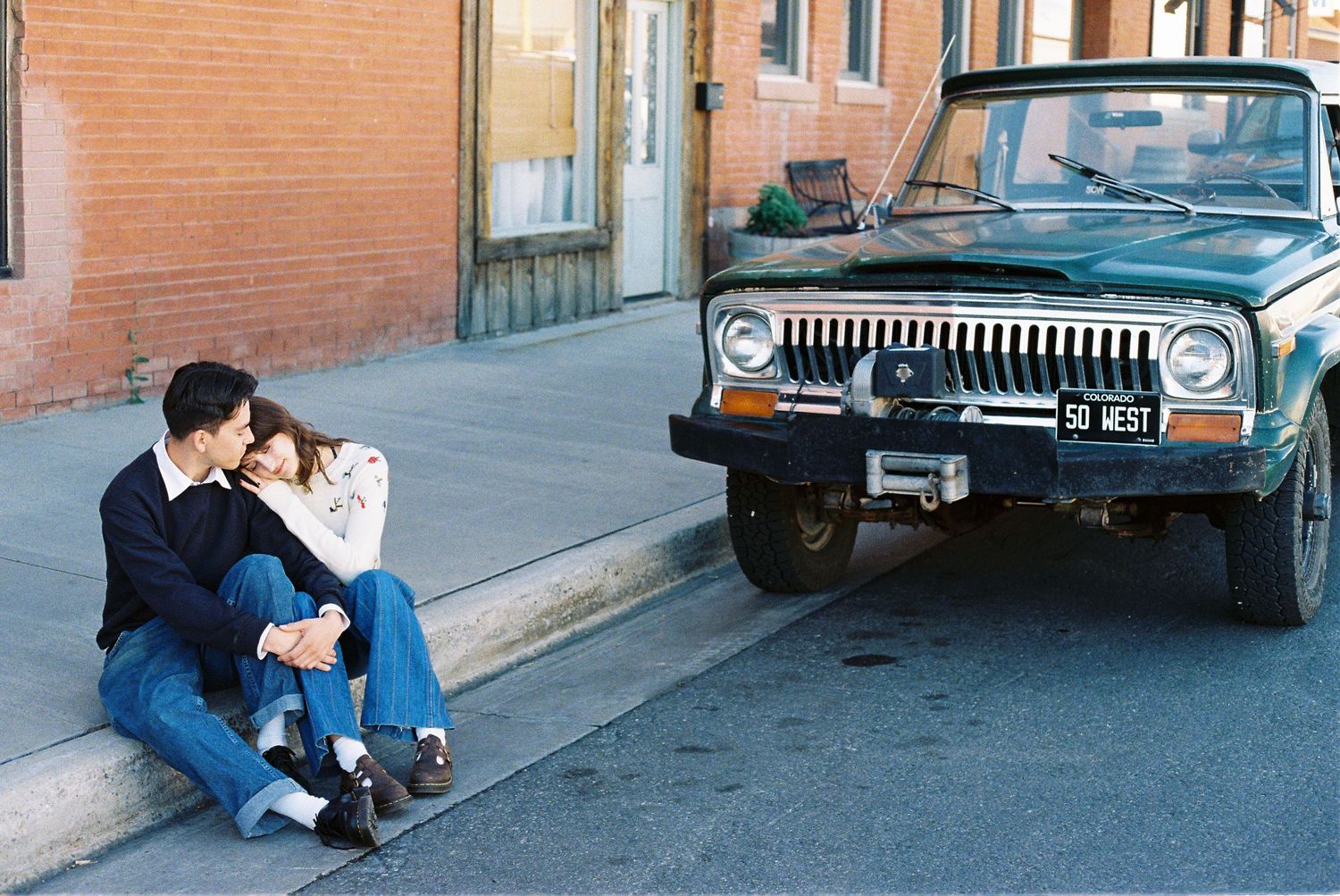 A tender moment shared between people sitting by a vintage Jeep on a city street.