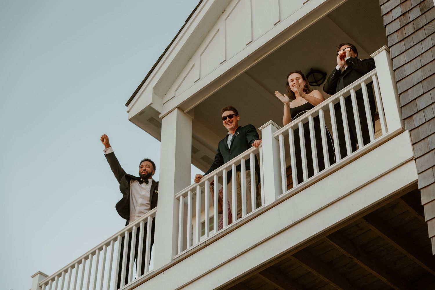 Wedding party celebrates on a white balcony of a coastal house.