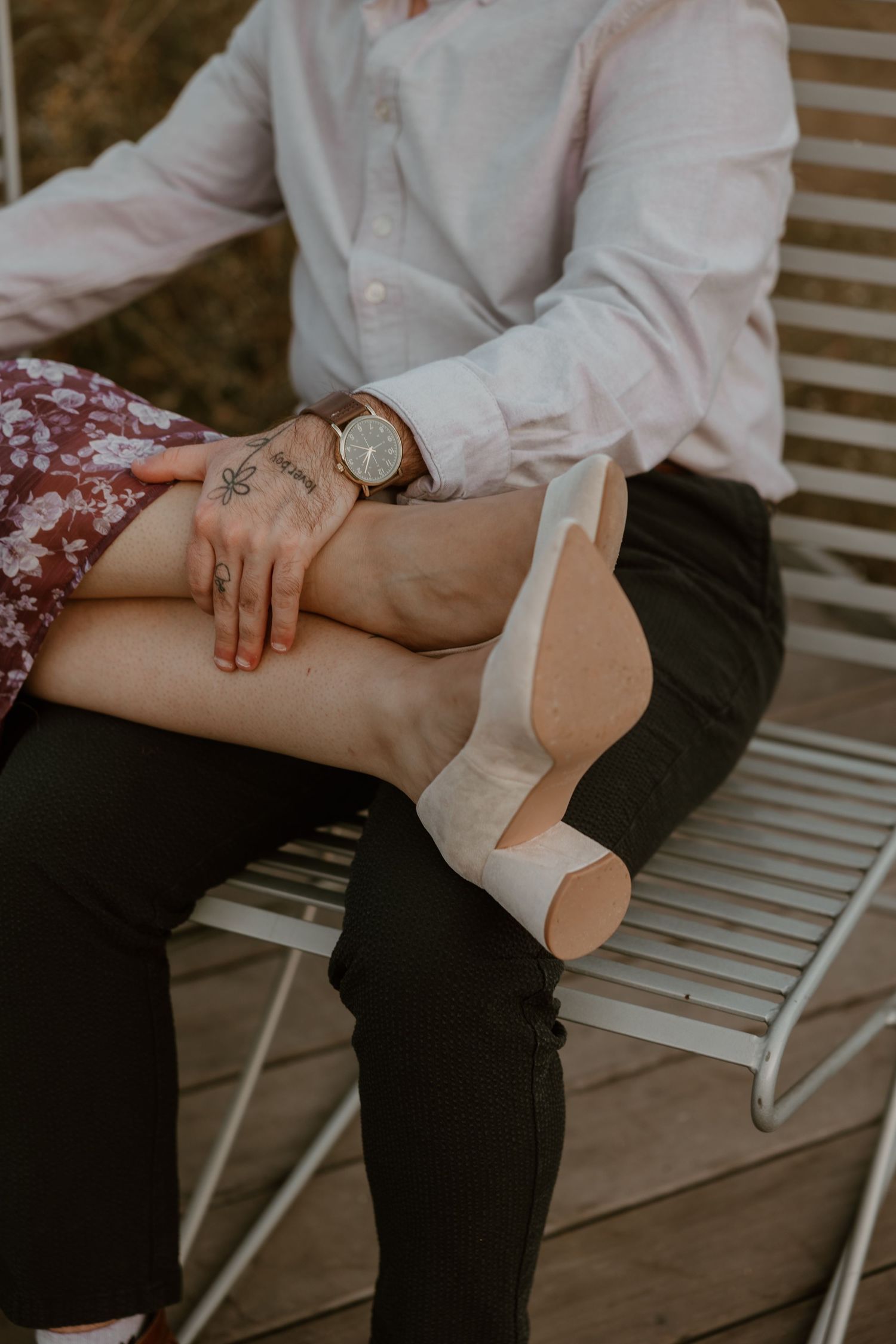 Close-up of hands and legs on white bench showing intimate moment between couple.