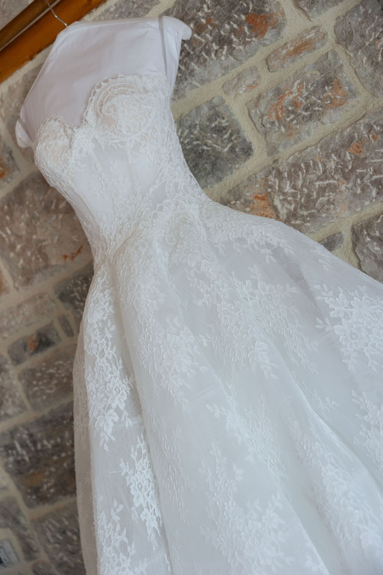 Close-up details of delicate white lace and tulle fabric from a wedding dress against a stone wall background.