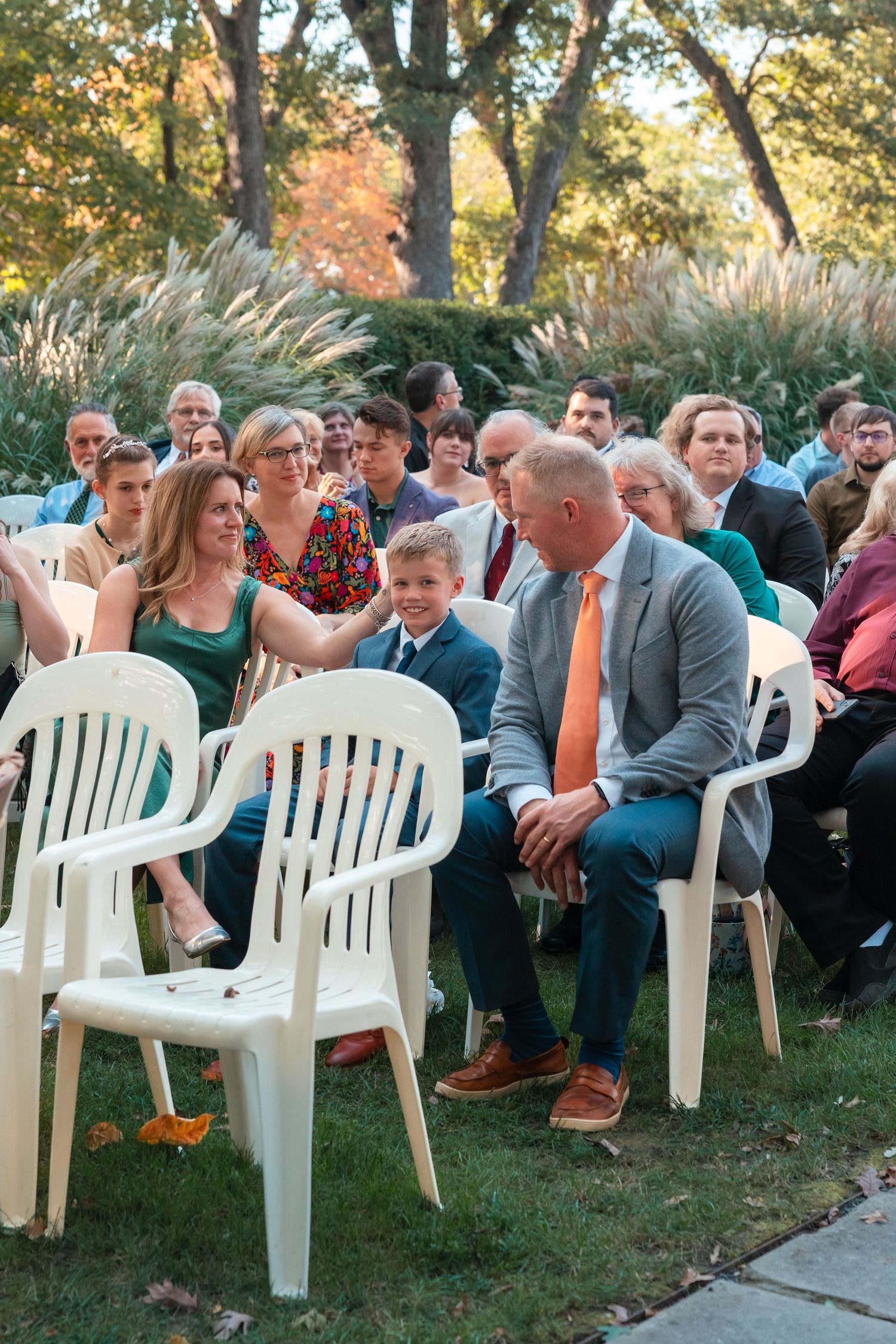 Outdoor wedding ceremony setup with white plastic chairs on grass during autumn.