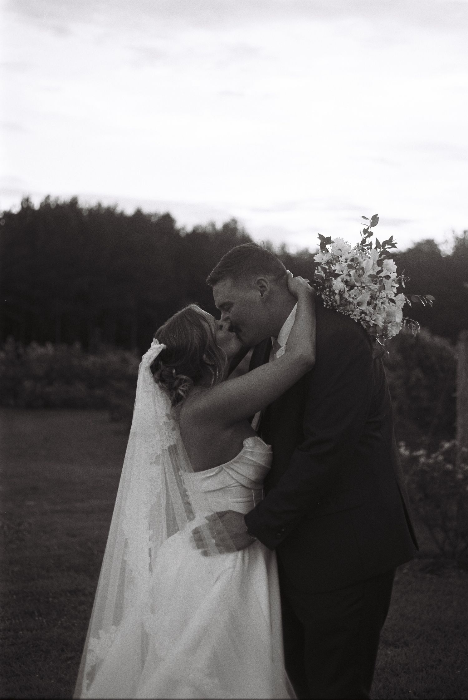 A romantic black and white wedding photo sequence showing a couple embracing and kissing in an outdoor setting.