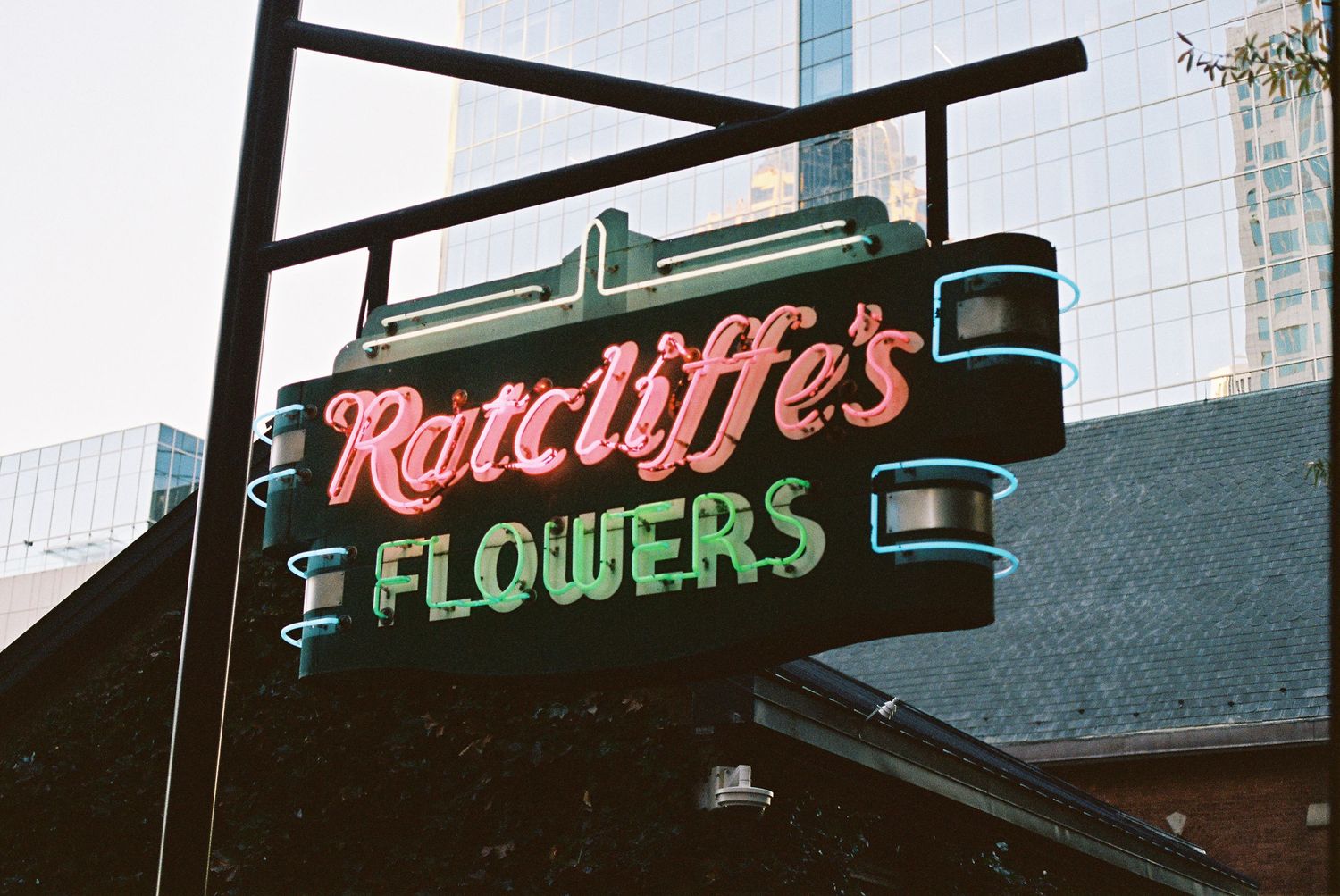 Vintage neon sign for Ratcliffe's Flowers illuminated against a dark building exterior.