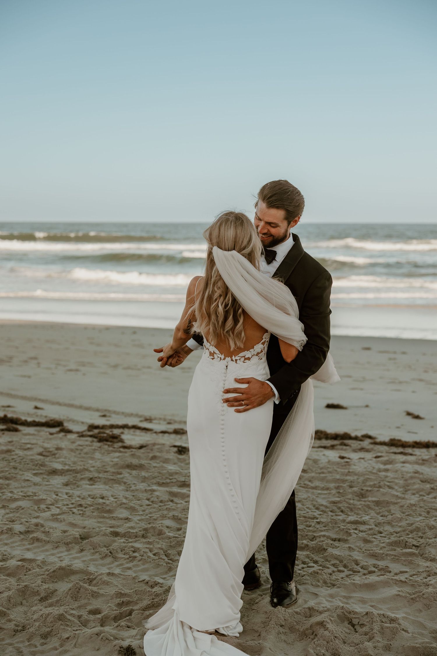 A romantic embrace between newlyweds on a sandy beach with ocean waves in the background.