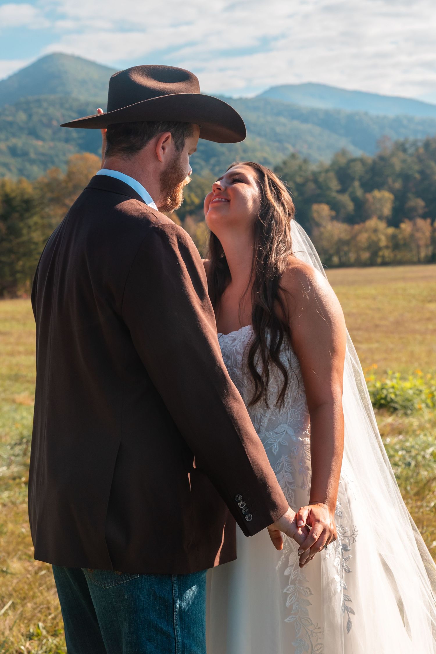 Wedding couple poses in a scenic mountain meadow with rolling hills in the background.
