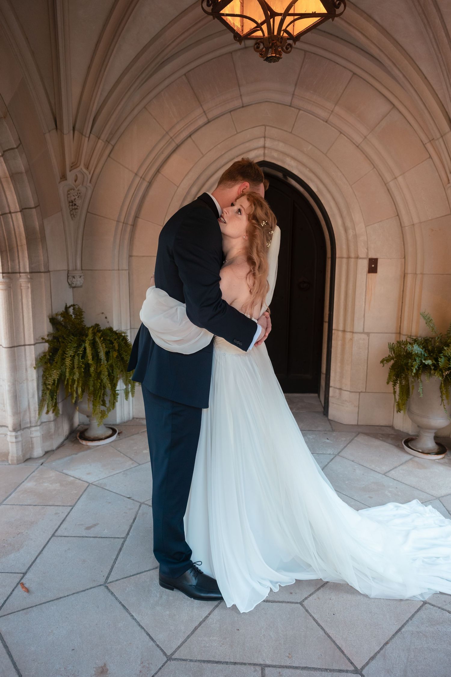 Elegant white wedding dress train flows across stone archway floor in romantic setting.