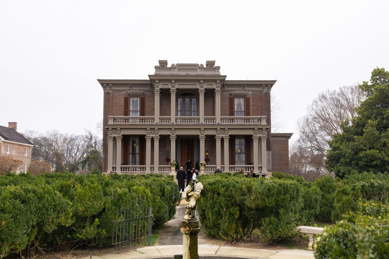 Historic mansion with grand columns and stone facade stands amid lush gardens on a hilltop estate.