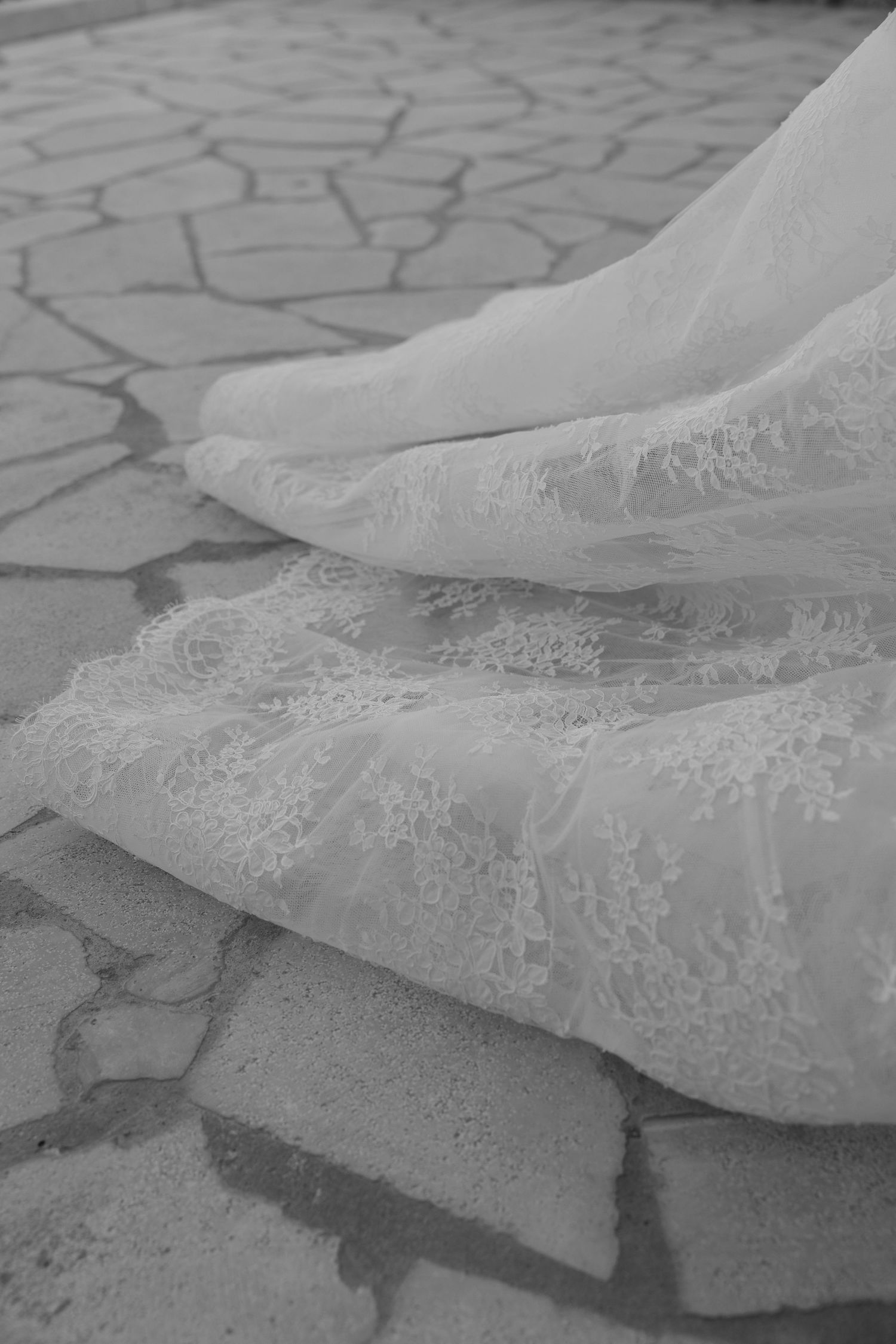 Intricate lace details of a flowing white wedding dress train on stone pavement.
