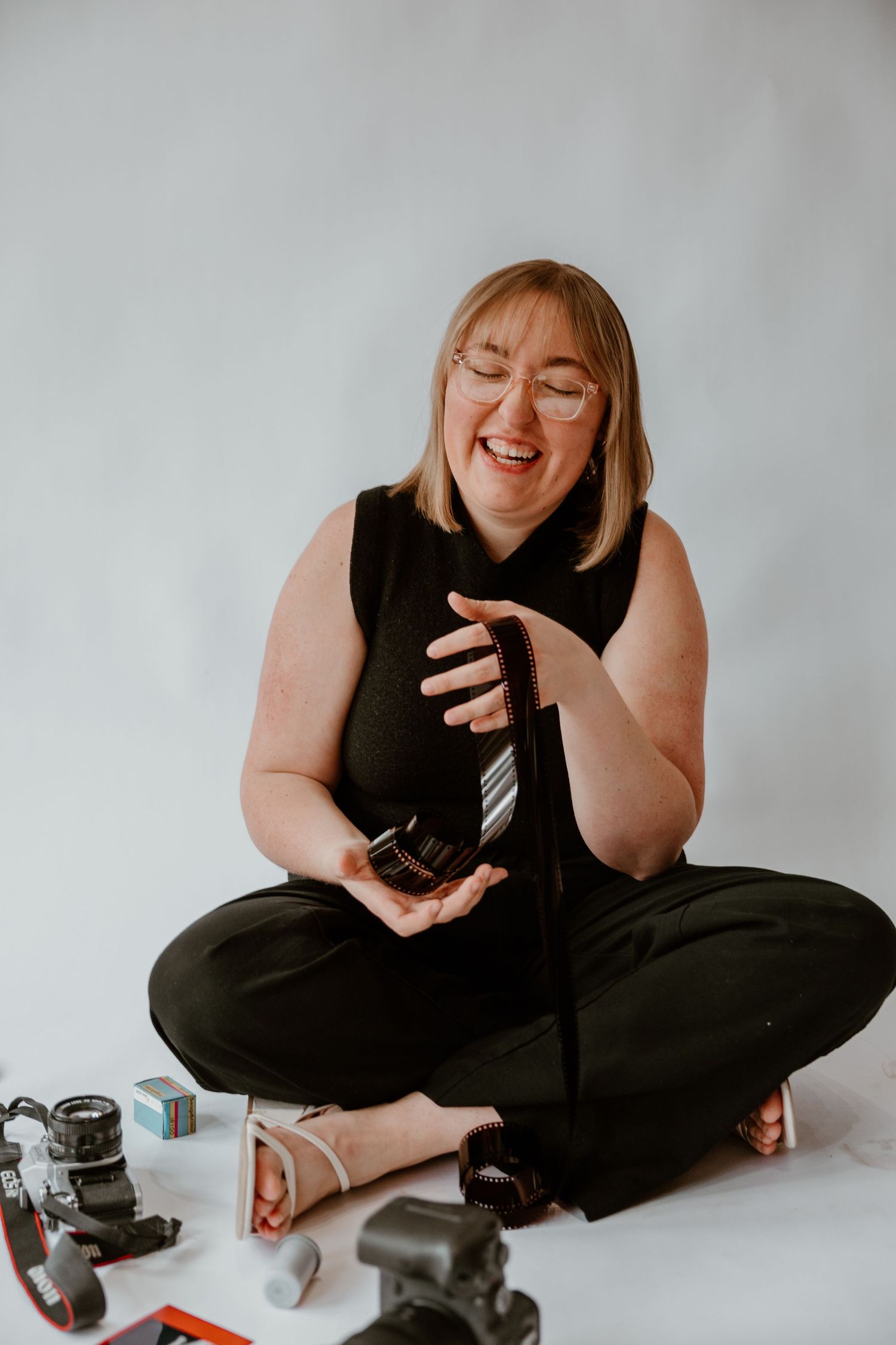 Photographer smiles and relaxes during creative self-portrait session with camera equipment on studio floor.