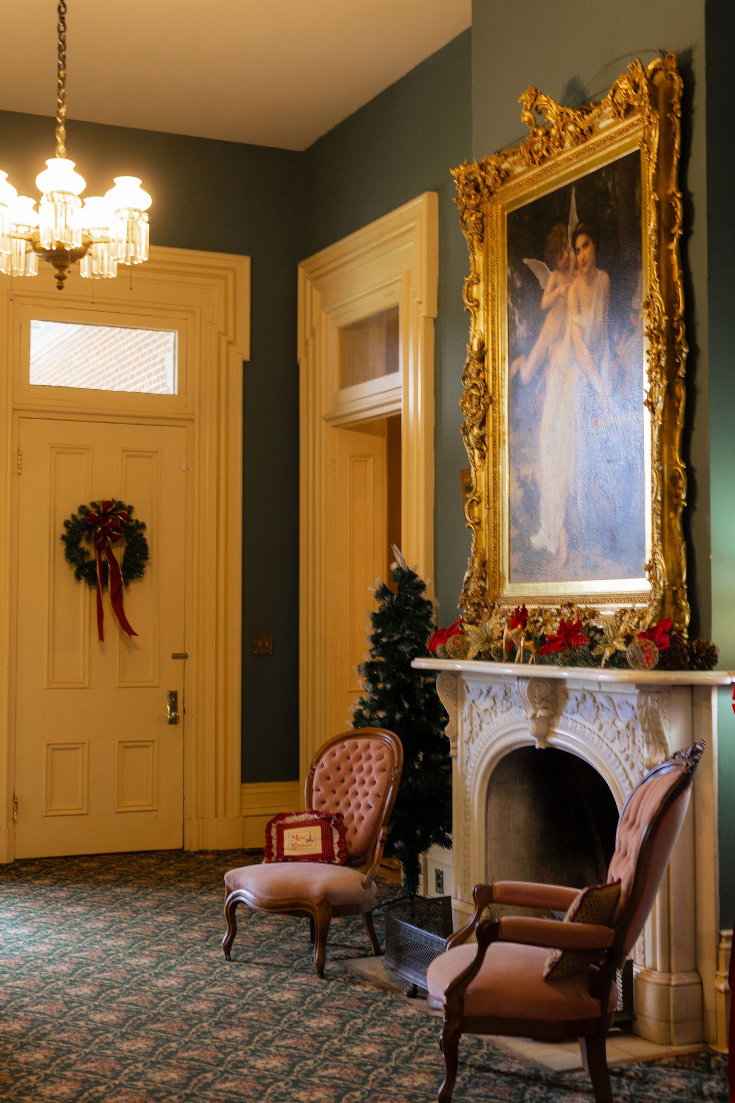 Elegant Victorian parlor with ornate gold frames, crystal chandeliers, and vintage upholstered chairs on patterned carpet.