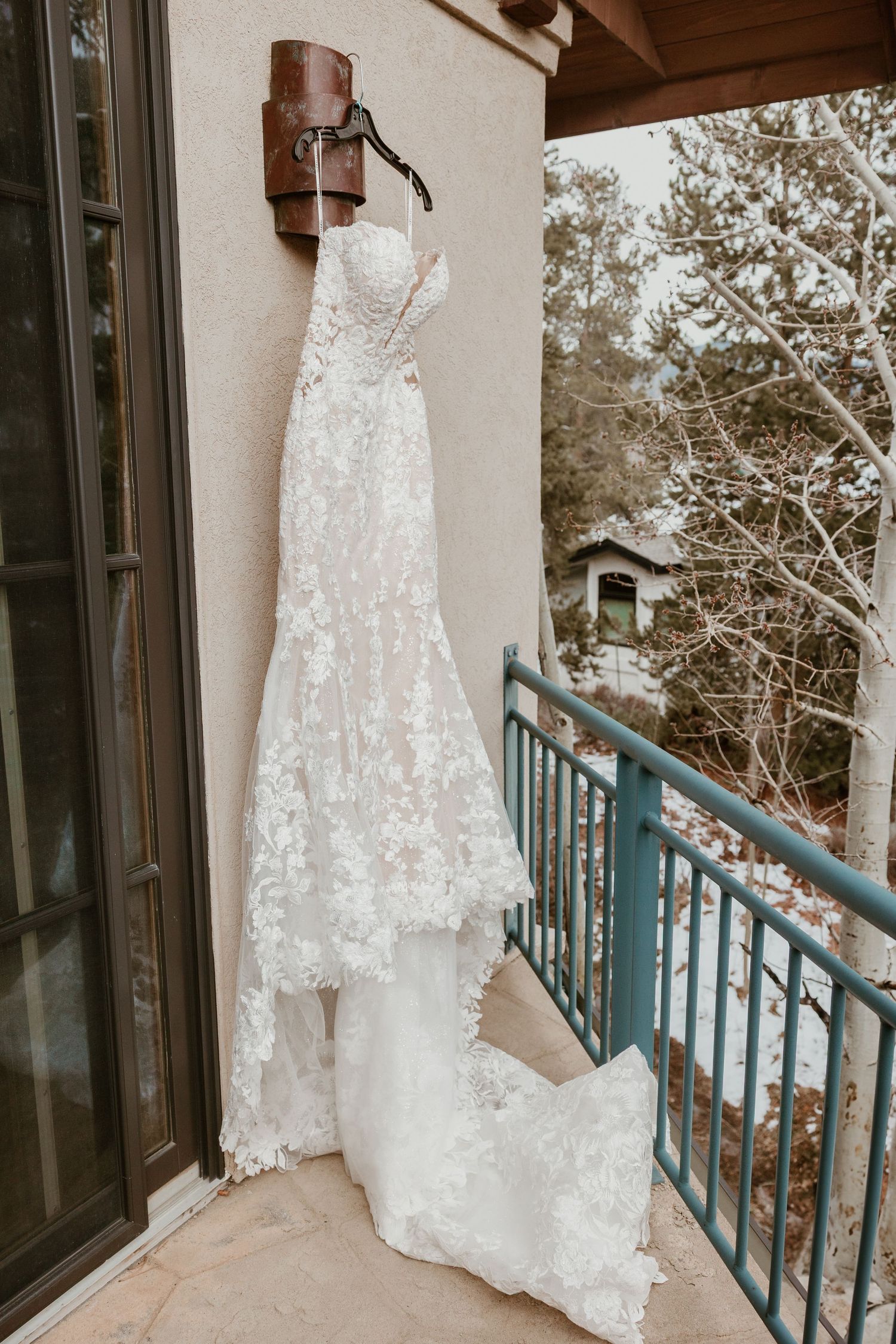 An elegant white lace wedding dress hangs on display on an outdoor balcony.