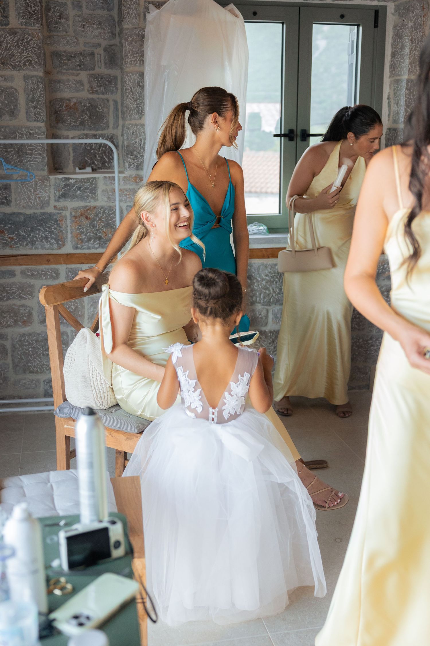 Wedding party members in yellow bridesmaid dresses and a white flower girl dress gather during pre-ceremony preparations.