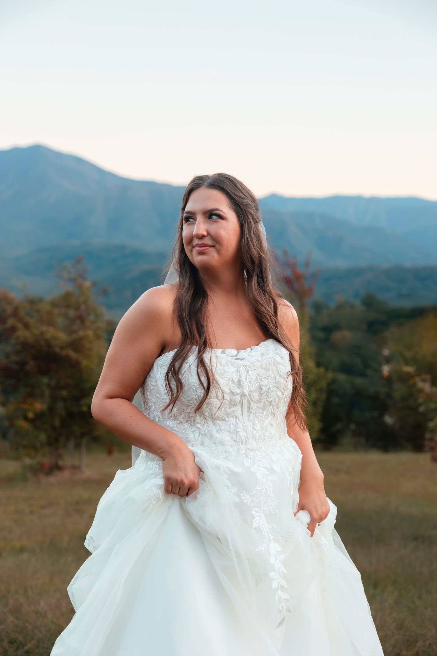 A bridal photoshoot in a scenic mountain field with a flowing white lace wedding dress.