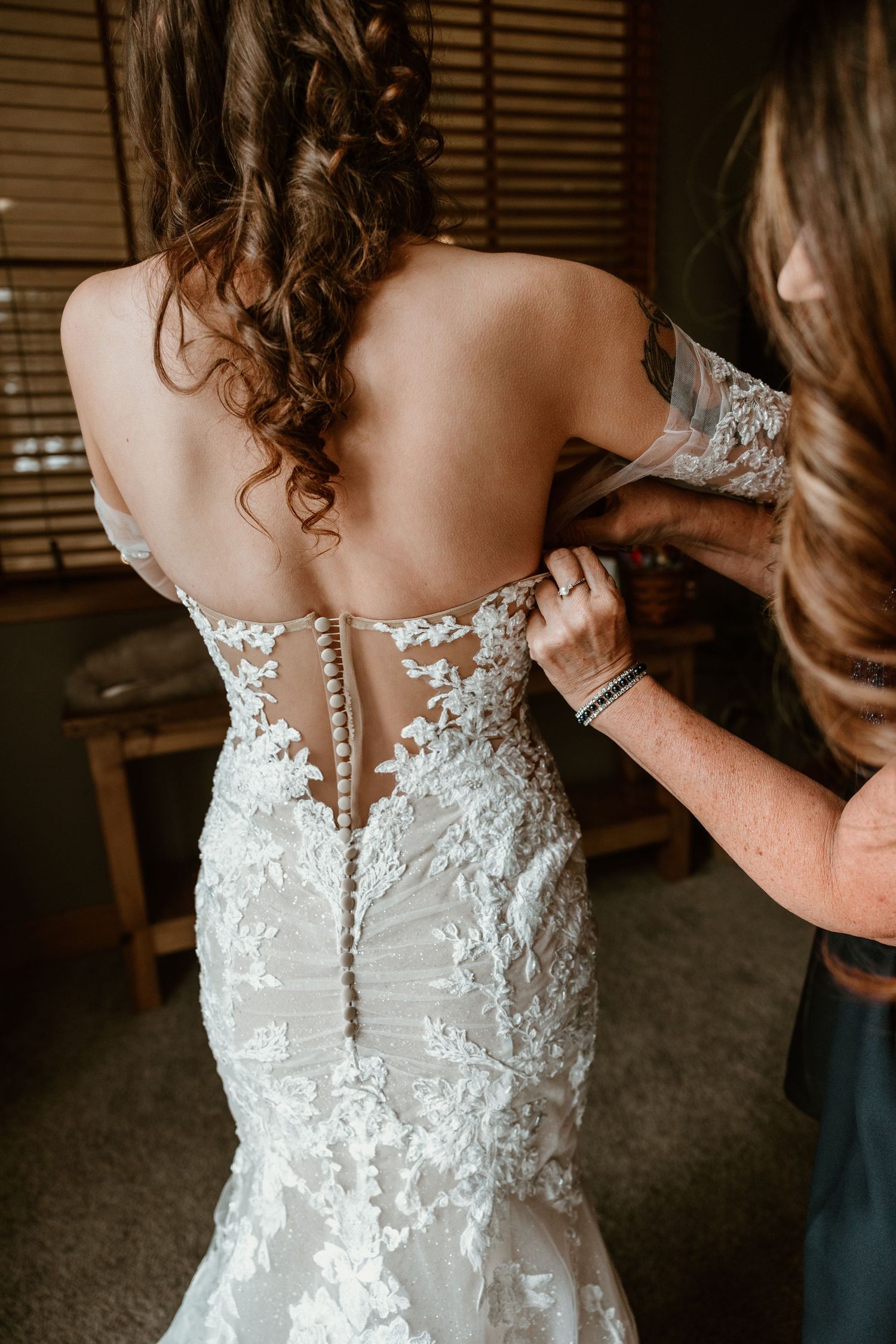 Close-up of intricate lace detailing and buttons on the back of a white wedding dress being fastened.