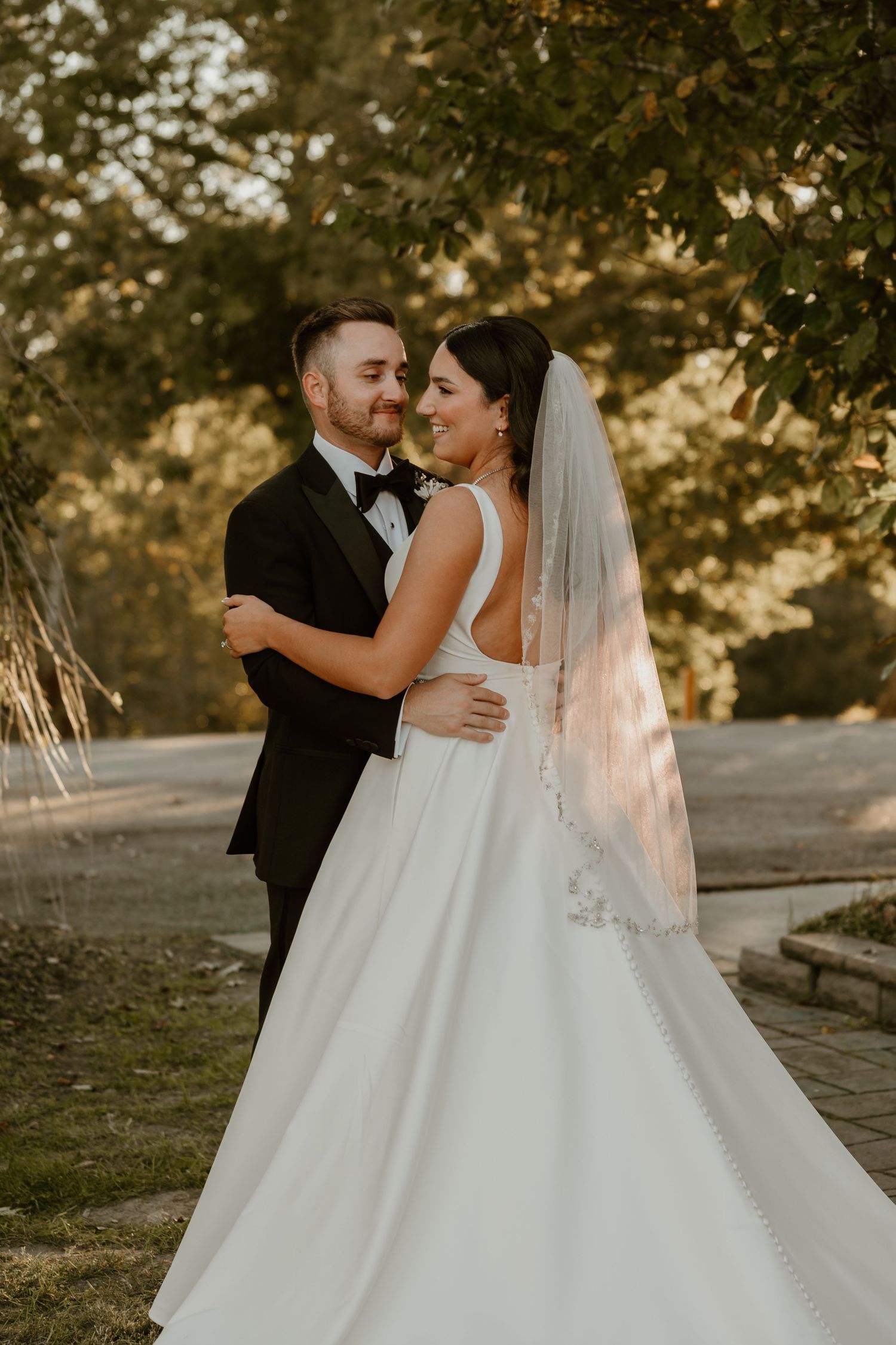 A romantic wedding portrait of a couple embracing outdoors in golden sunlight.