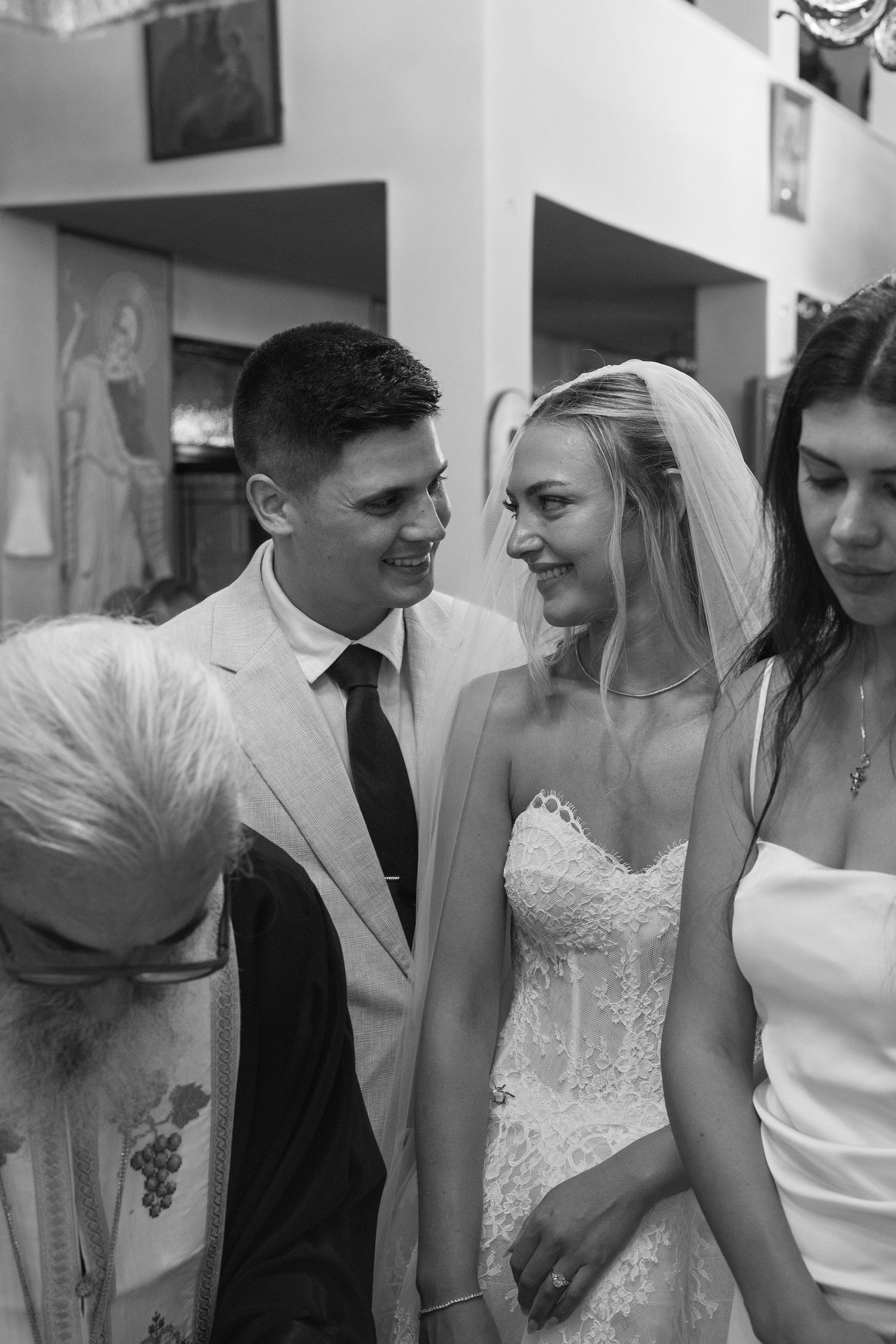 Wedding party interacts and smiles during a candid moment inside a church with religious artwork visible.