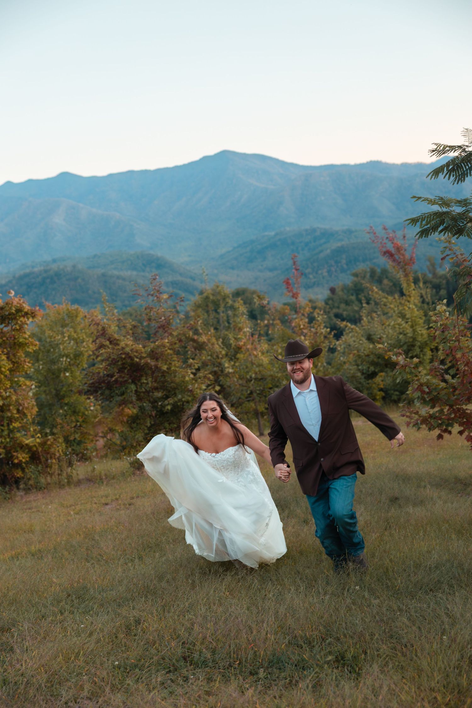 A couple dances playfully in a mountain meadow at sunset with the bride's dress flowing in the wind.