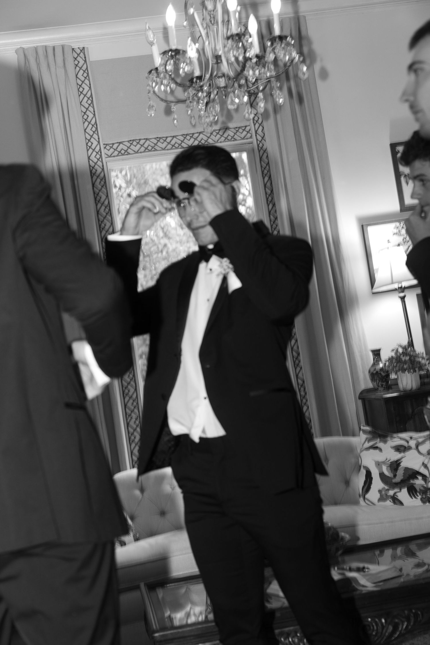 Black and white photo of wedding preparations in an elegant room with chandelier.