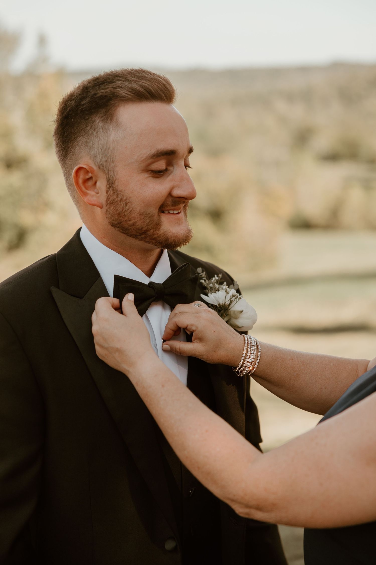 Close-up shot of boutonniere being pinned on formal black tuxedo.