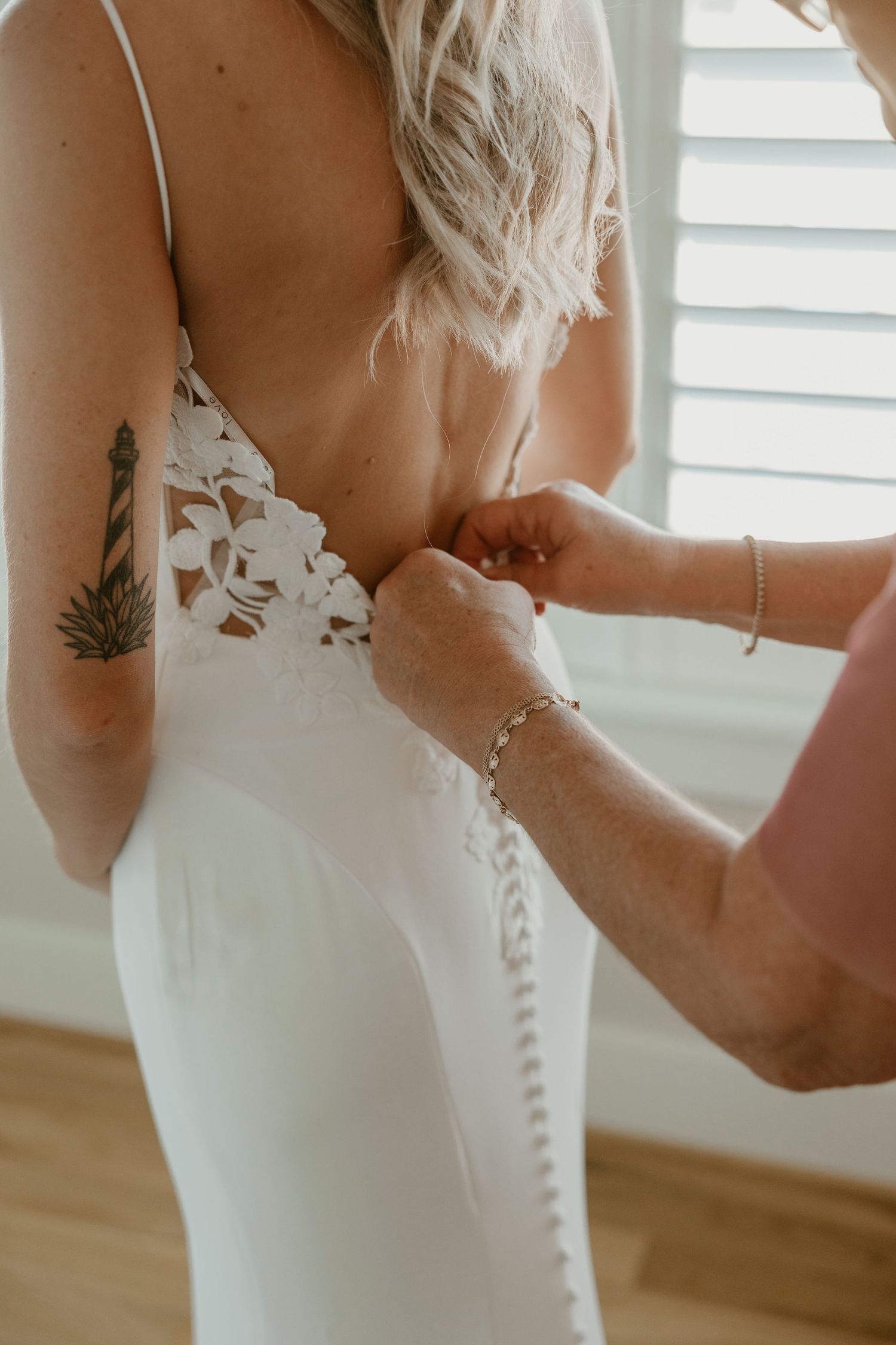 Close up of buttons being fastened on back of white wedding dress with lighthouse tattoo visible.
