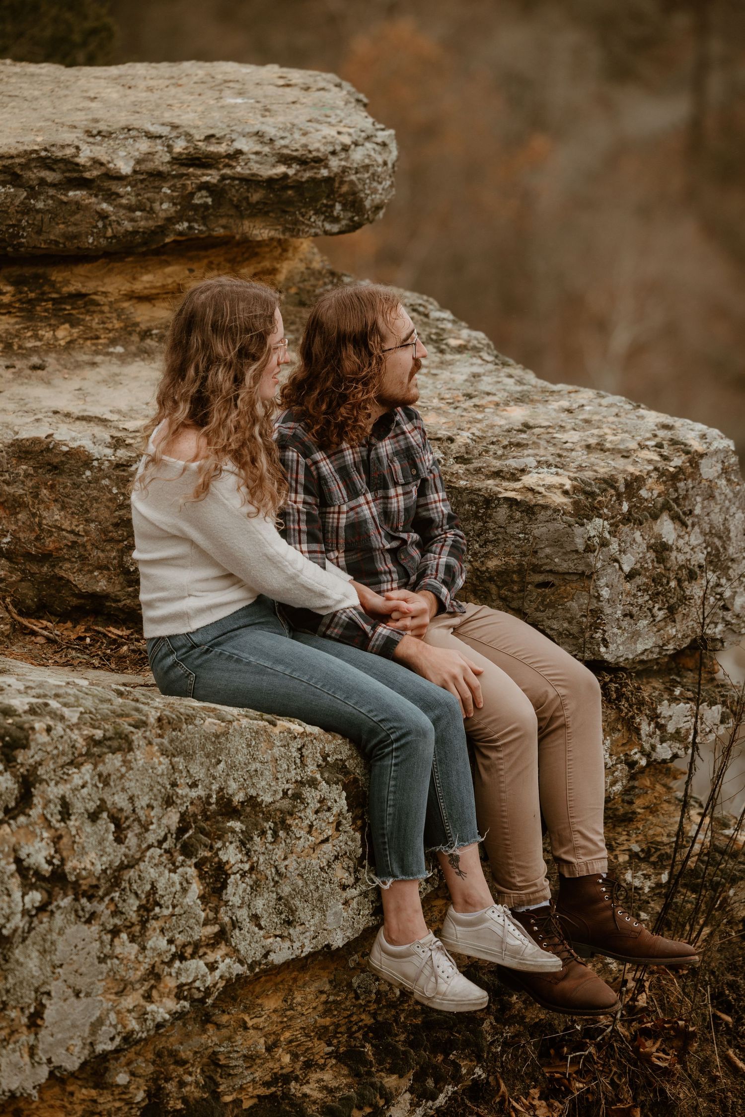 Couple sitting together on large rock formation with scenic mountain vista.