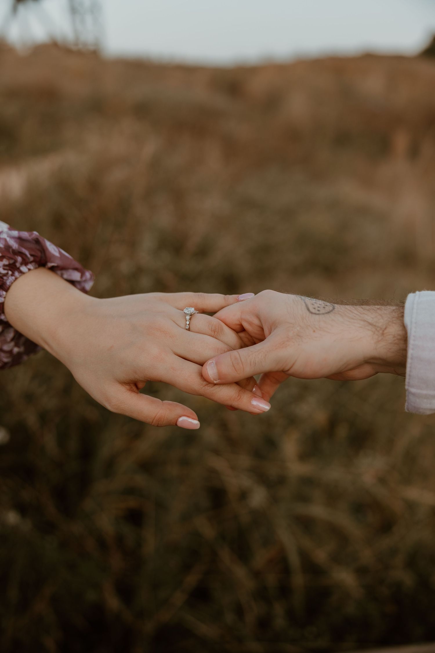 Close-up of hands tenderly touching showing engagement ring in natural outdoor setting.