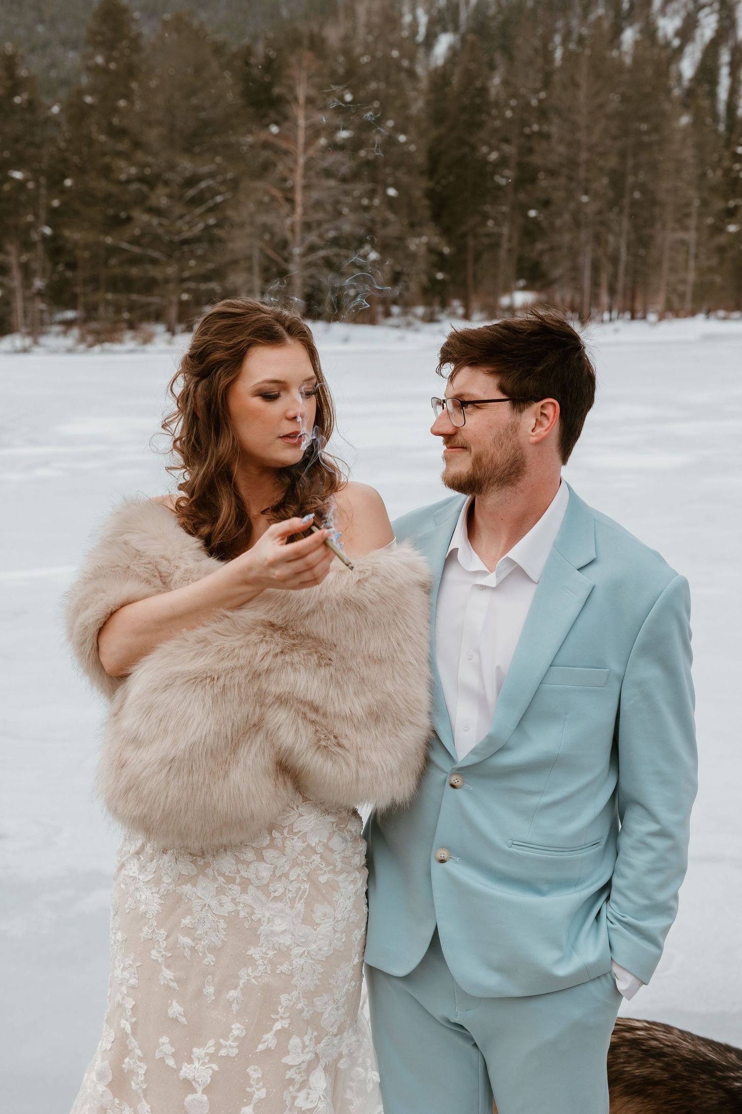 A bride in fur wrap and groom in light blue suit share an intimate moment in the snow.