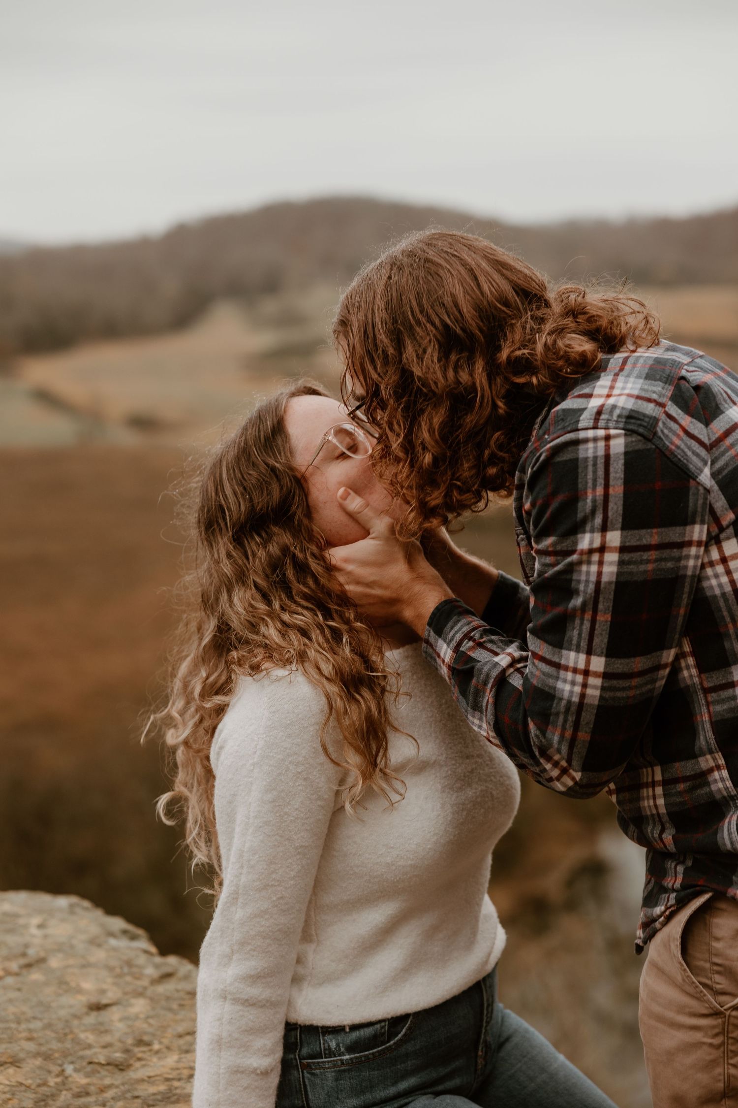 Romantic moment captured on clifftop with golden autumn landscape in background.