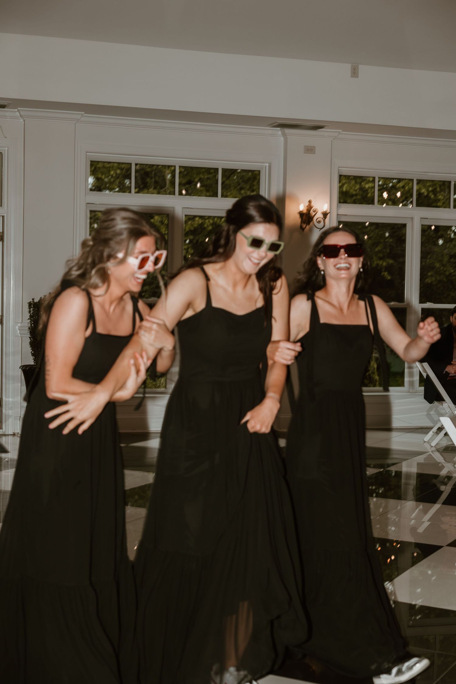 Bridesmaids in matching black dresses dancing at a wedding reception.