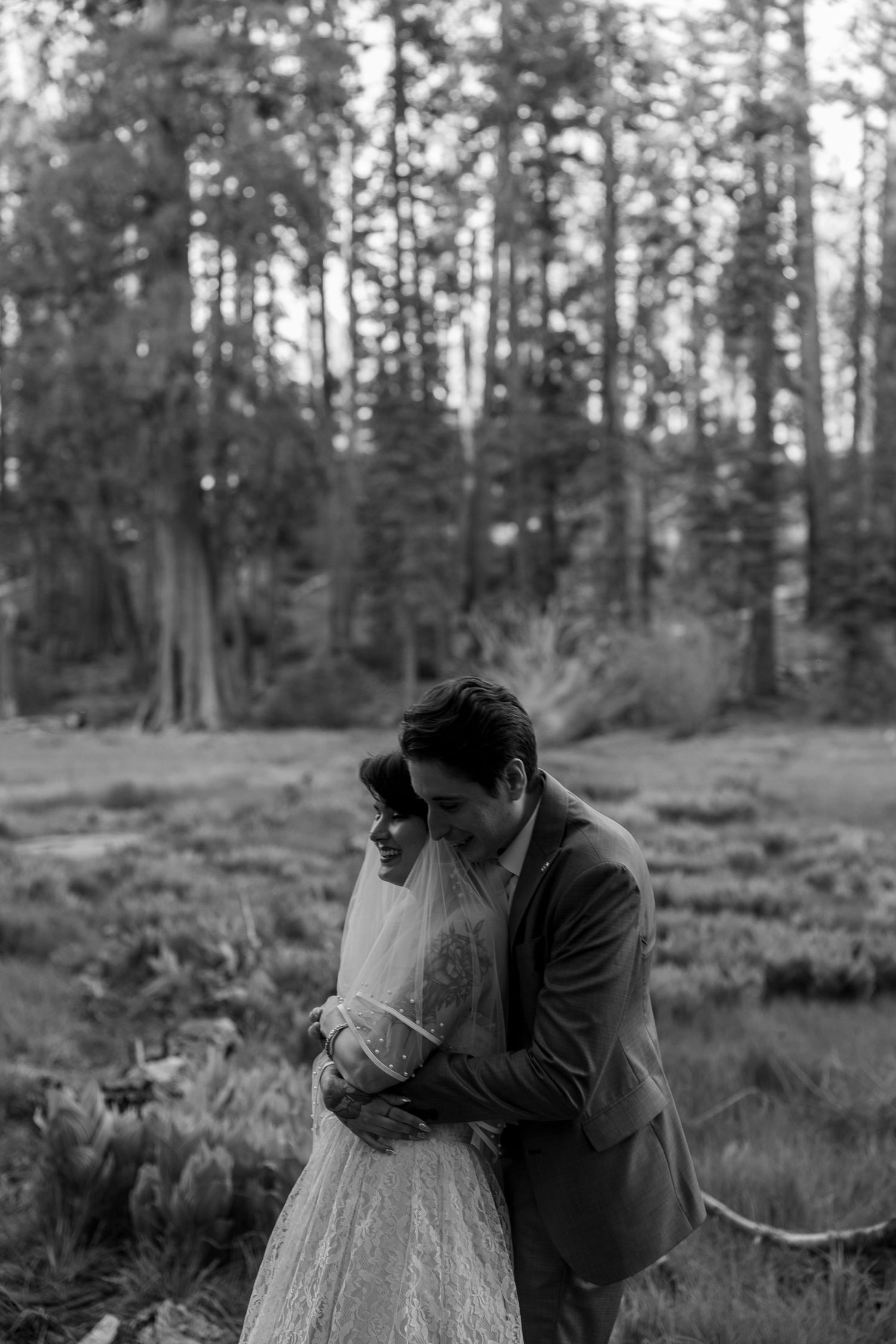 Black and white portrait of embracing newlyweds in forest meadow.