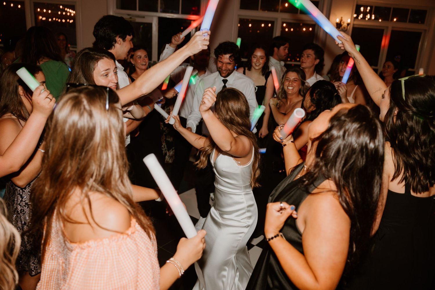 Wedding guests dancing with glowing light-up sticks on a dance floor.