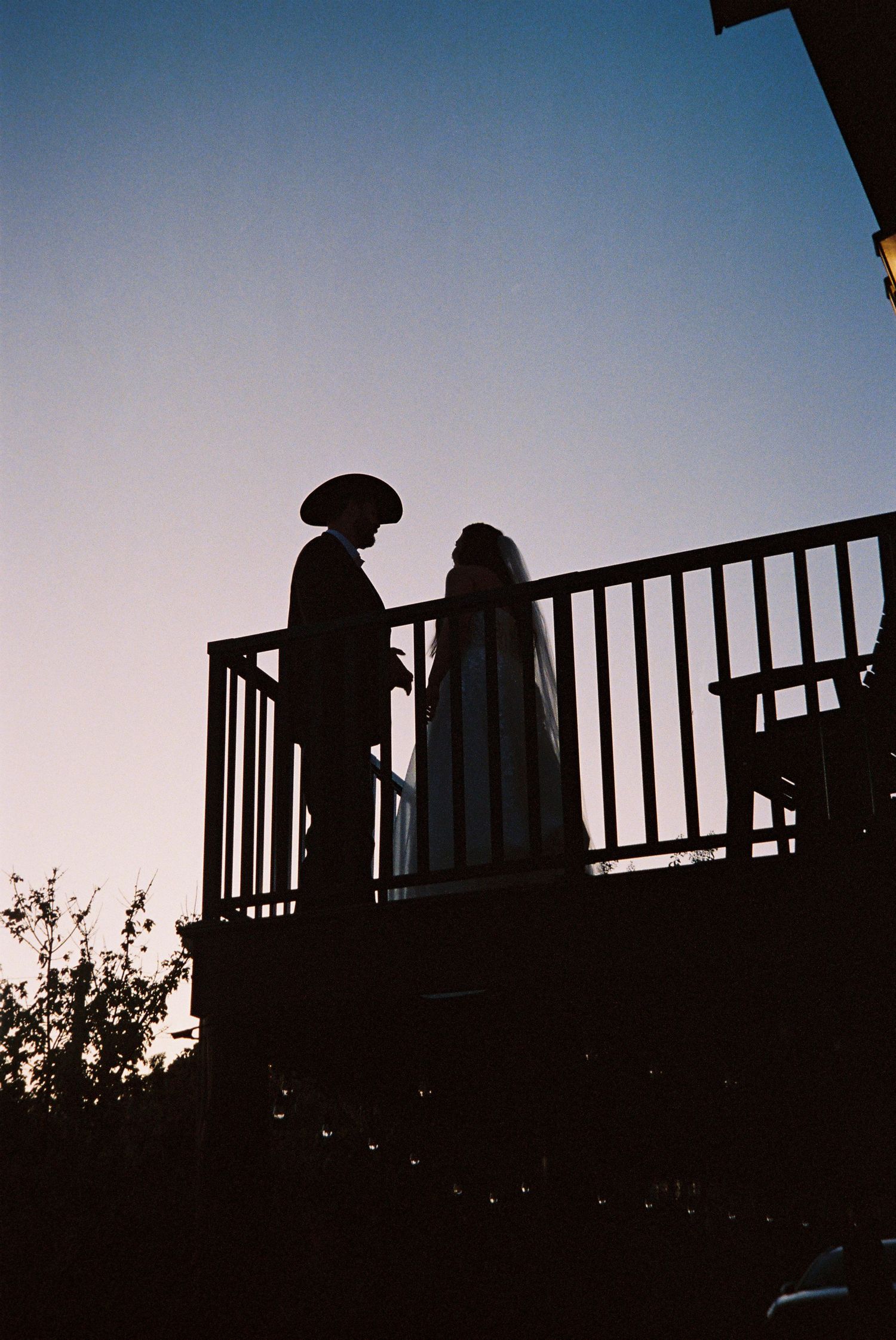 Silhouettes of people standing on a deck railing against a dusky sky during sunset.