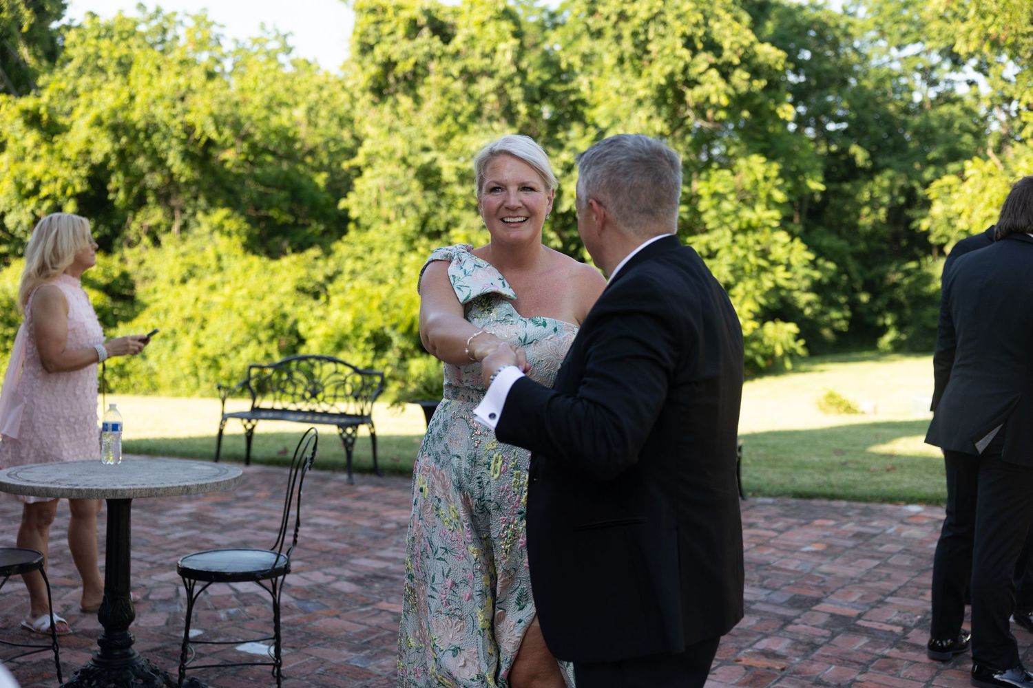 Outdoor wedding ceremony with guests gathered on brick patio surrounded by greenery.