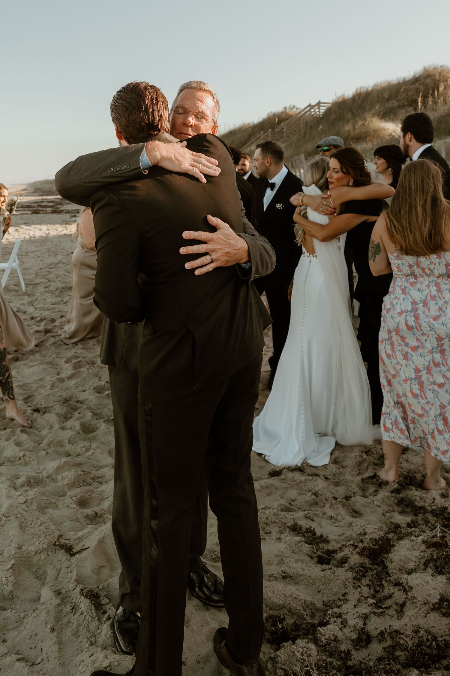Emotional embrace between wedding guests during beach celebration at sunset.
