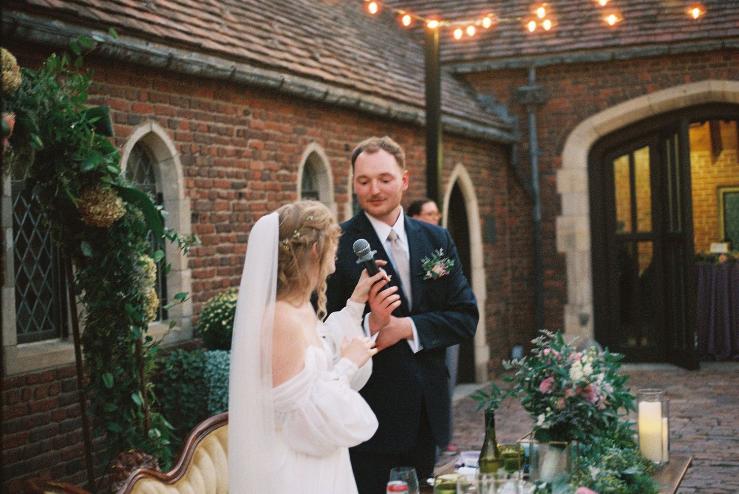 String lights illuminate a rustic brick courtyard during an evening wedding reception.