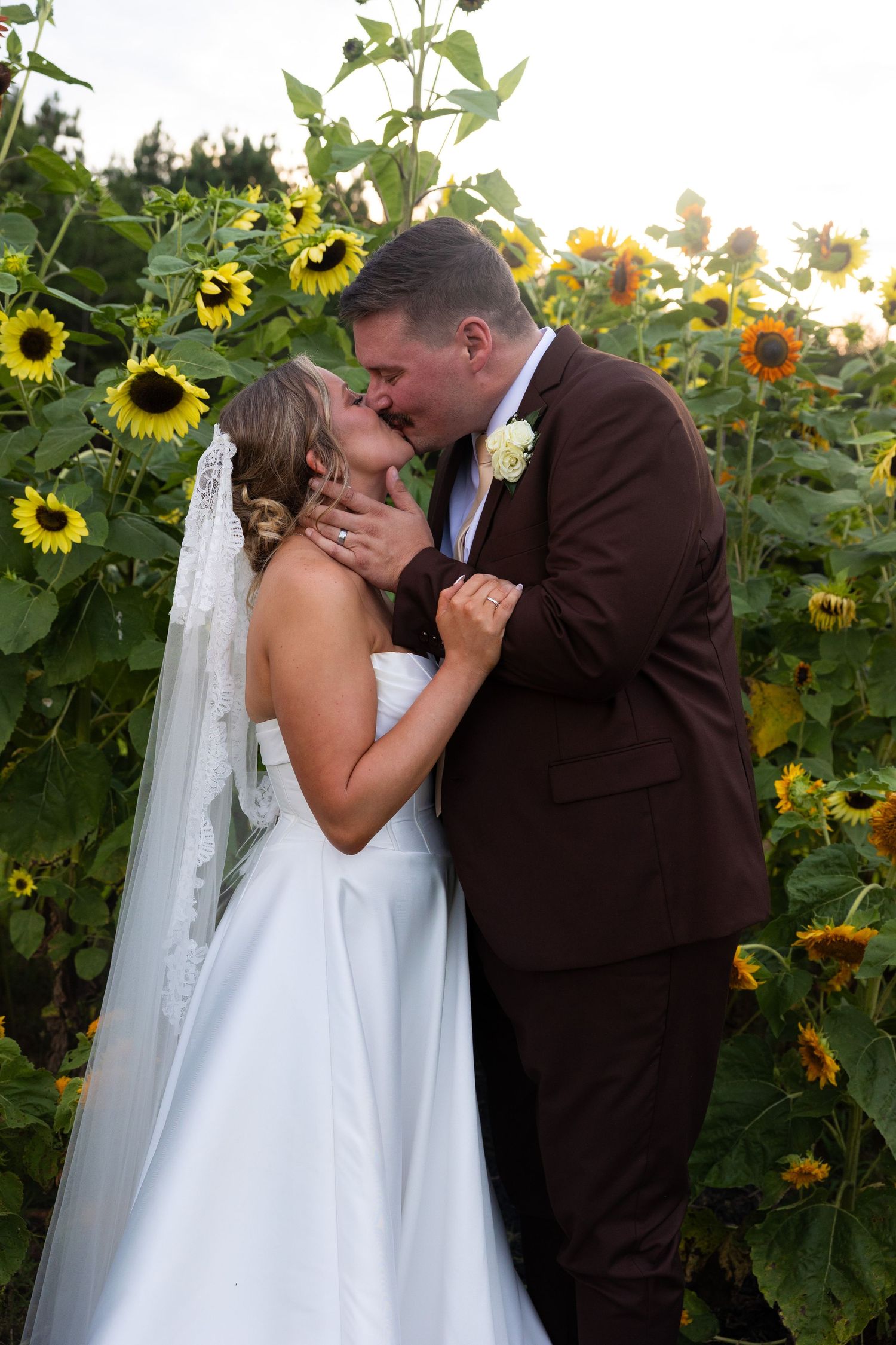 Romantic wedding moment captured in a sunflower garden at sunset.
