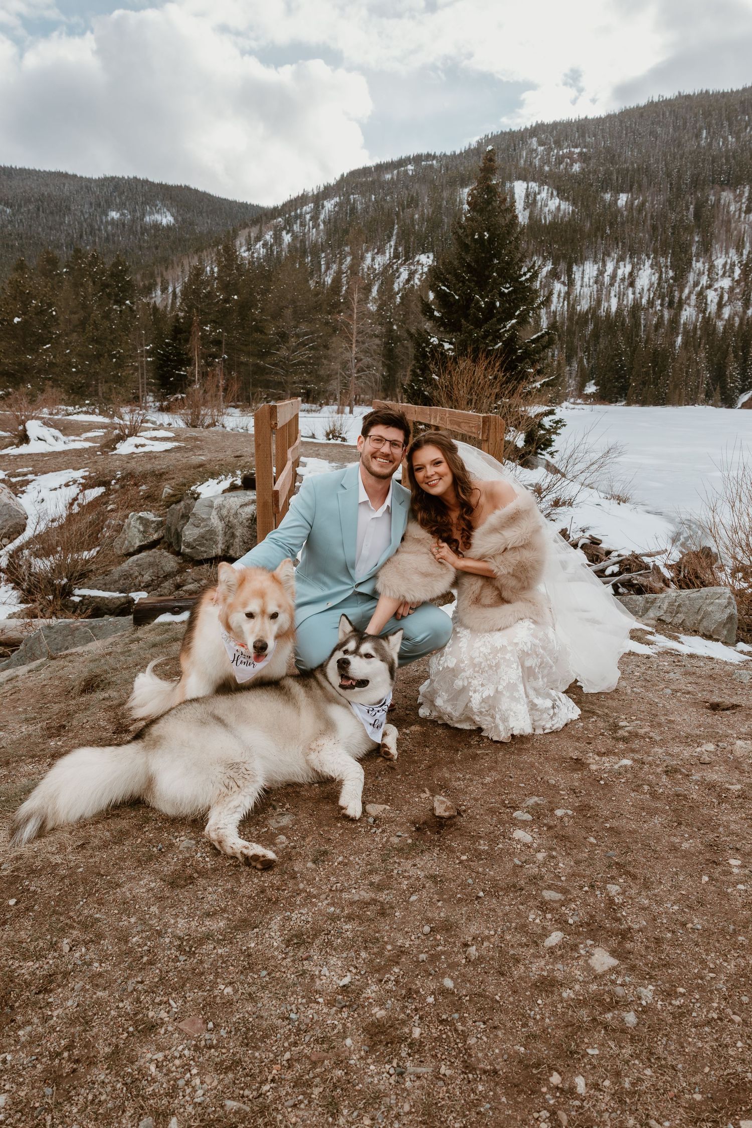 Wedding couple relaxes outdoors with their Husky dogs in a snowy mountain setting.
