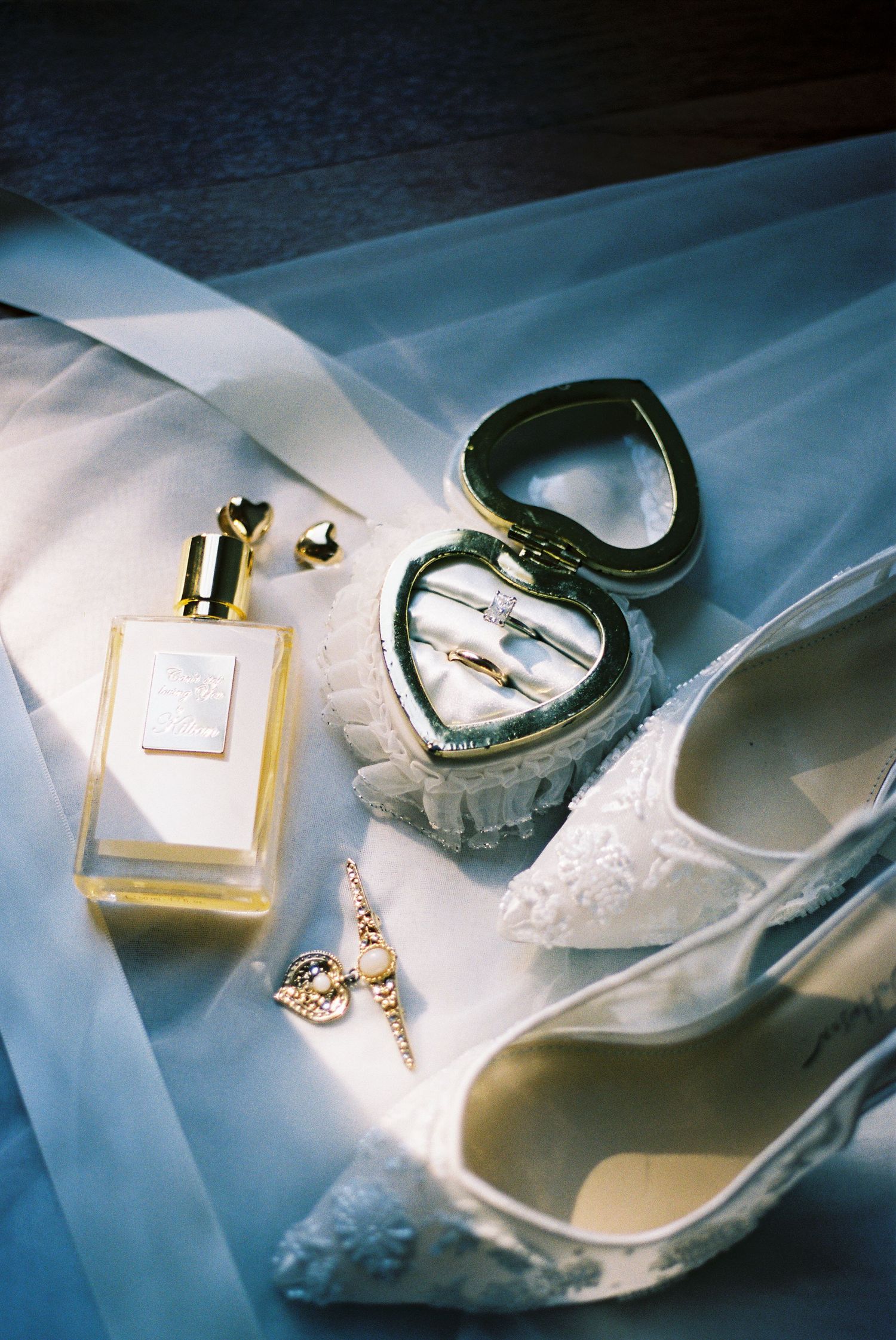 Wedding accessories including perfume, lace shoes, and jewelry arranged on blue fabric.