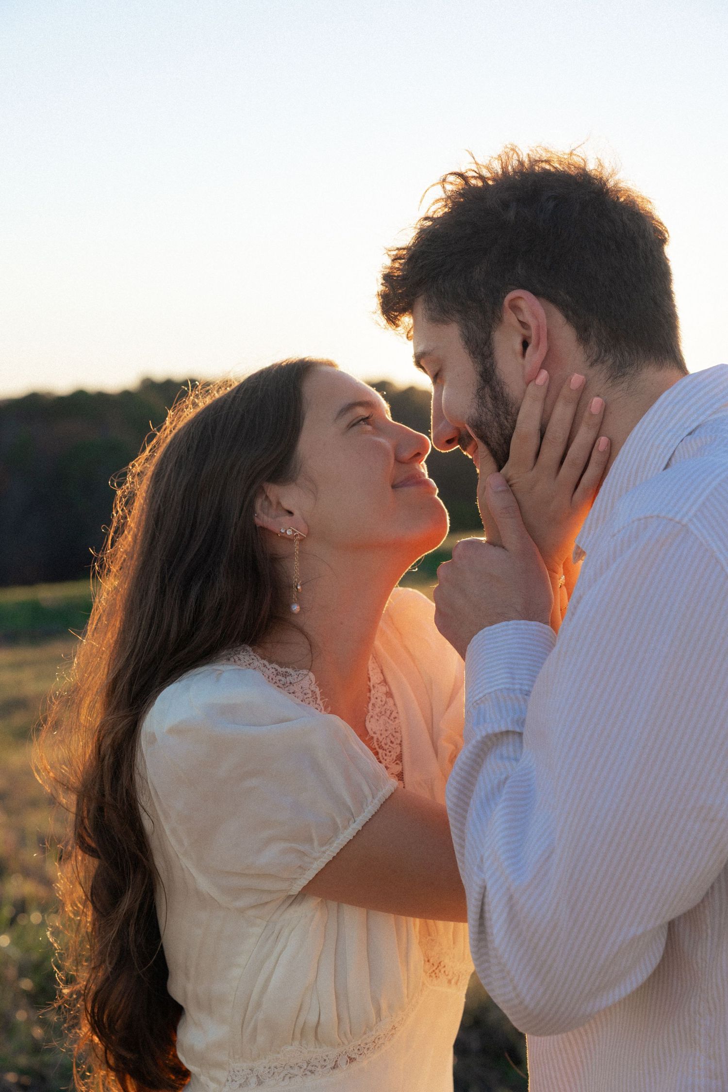 Romantic couple in white embraces closely during golden hour in a field.