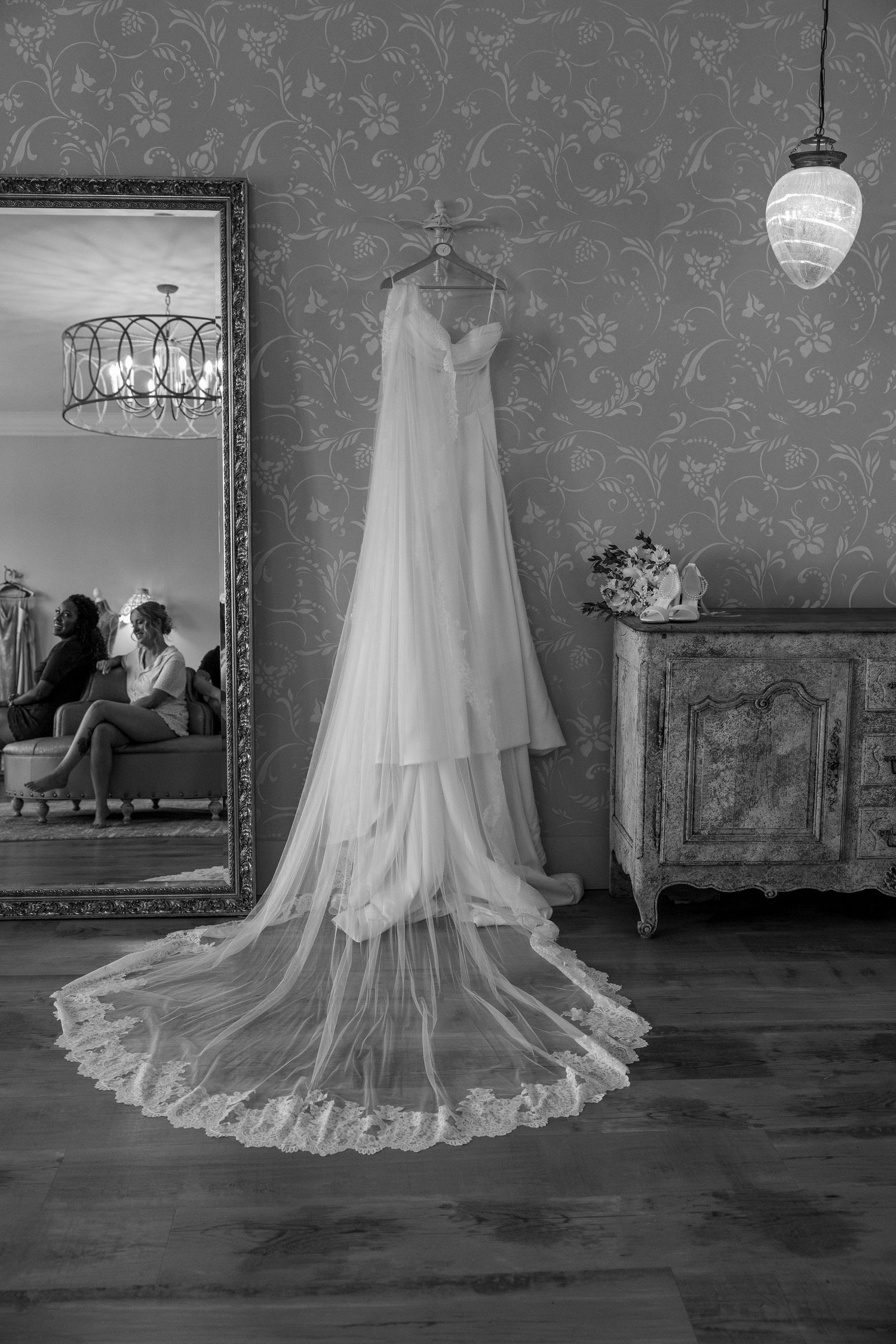 A series of elegant white wedding dresses displayed on hangers against a patterned gray wallpaper in a vintage room.