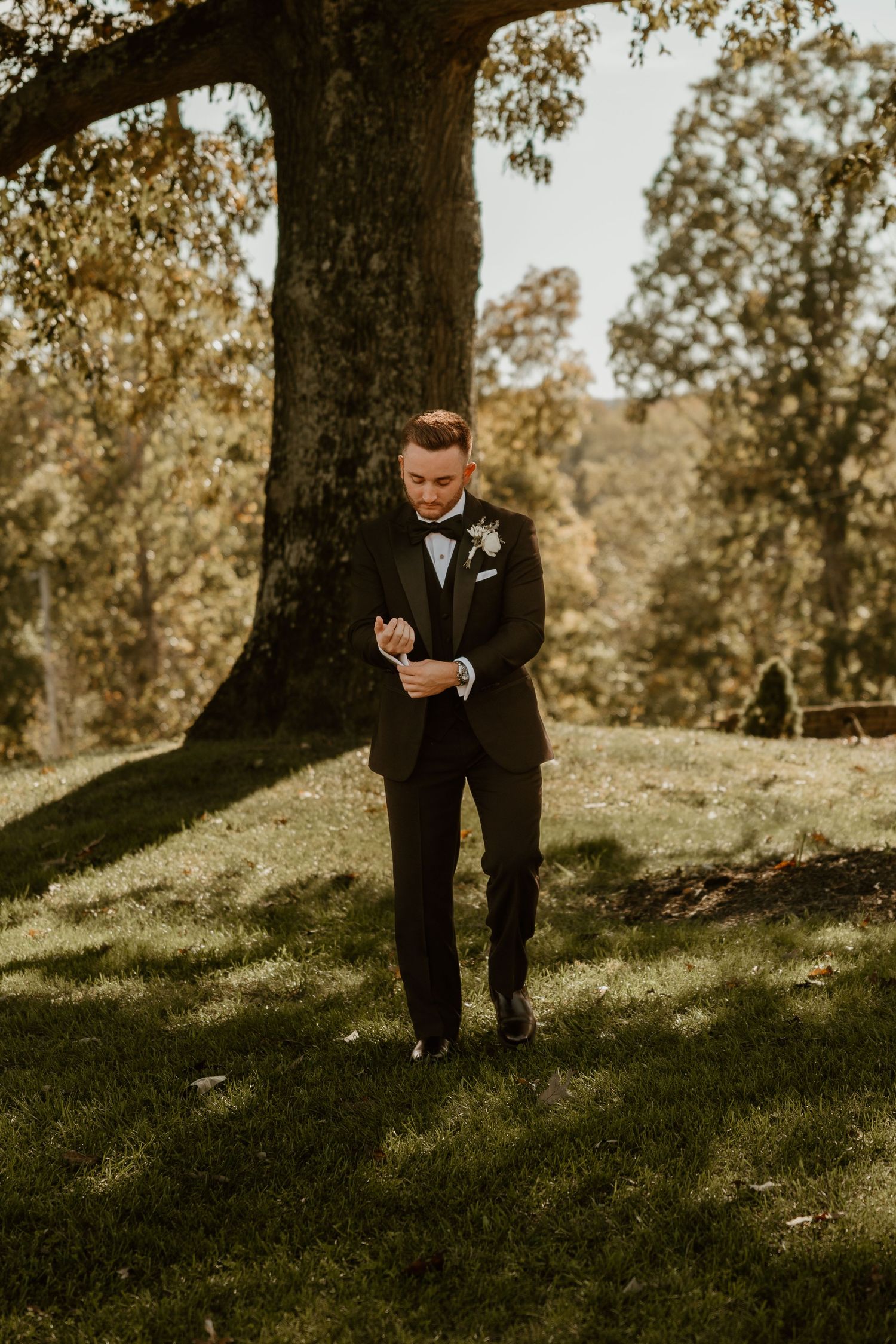 Person in formal attire standing under large tree during golden hour.