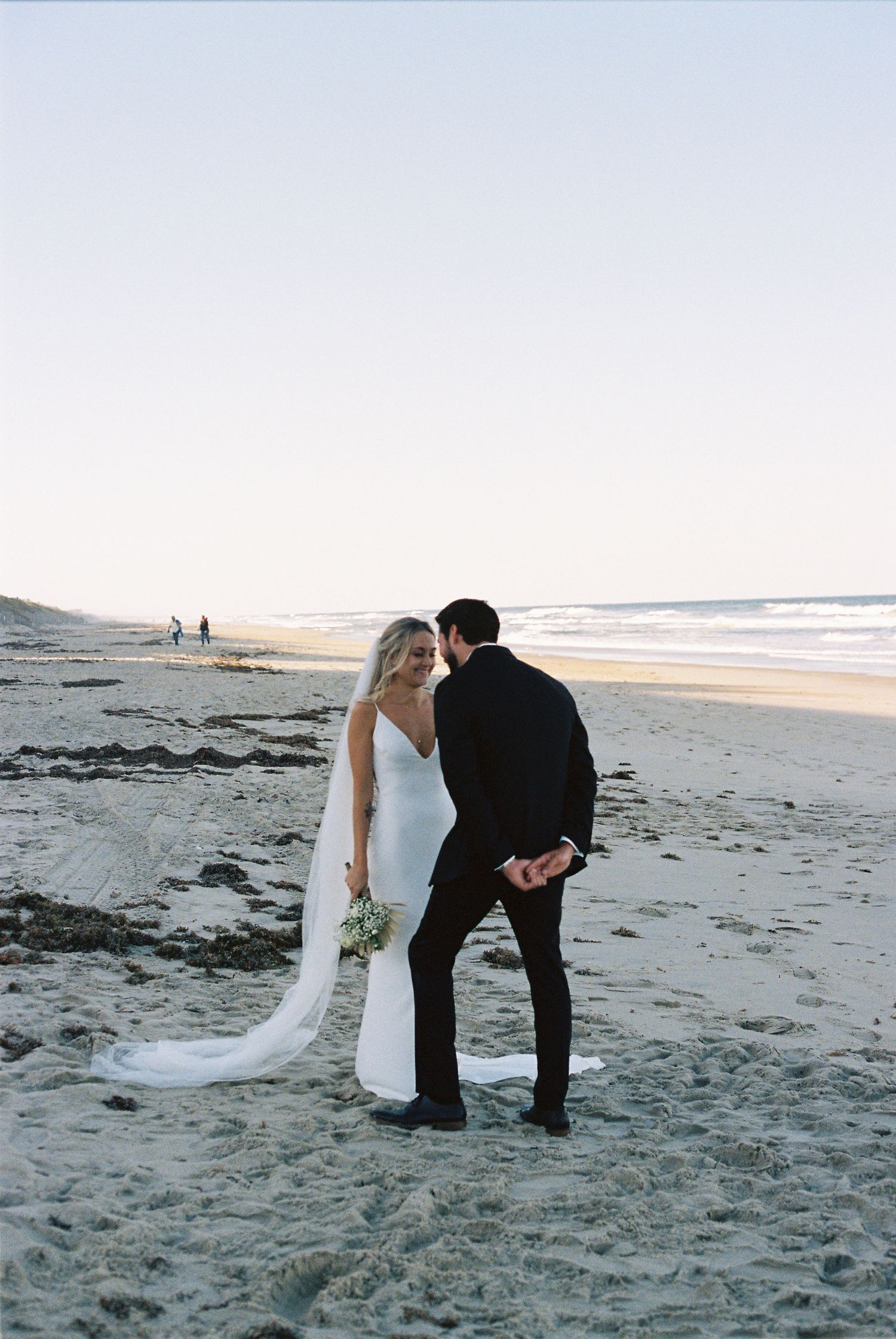 Romantic beach wedding photos with couple posing on sandy shore at sunset.