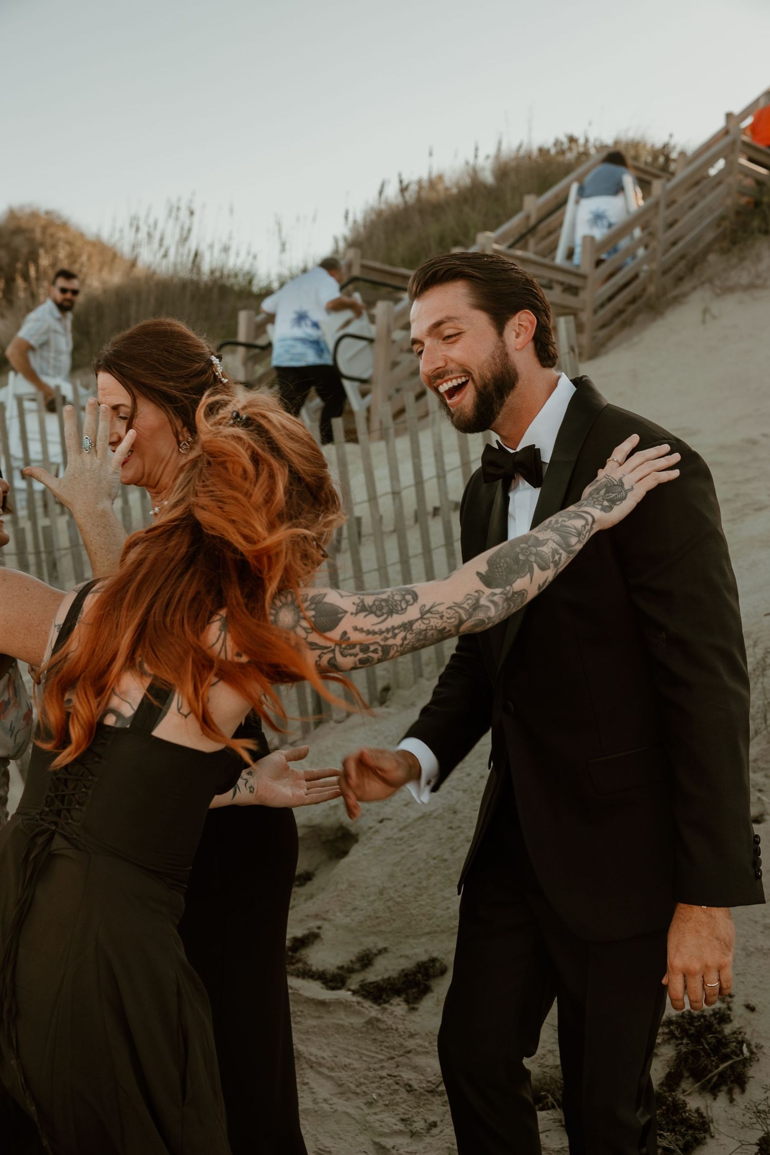 Joyful dancing and laughter during beach wedding celebration with wooden stairs in background.