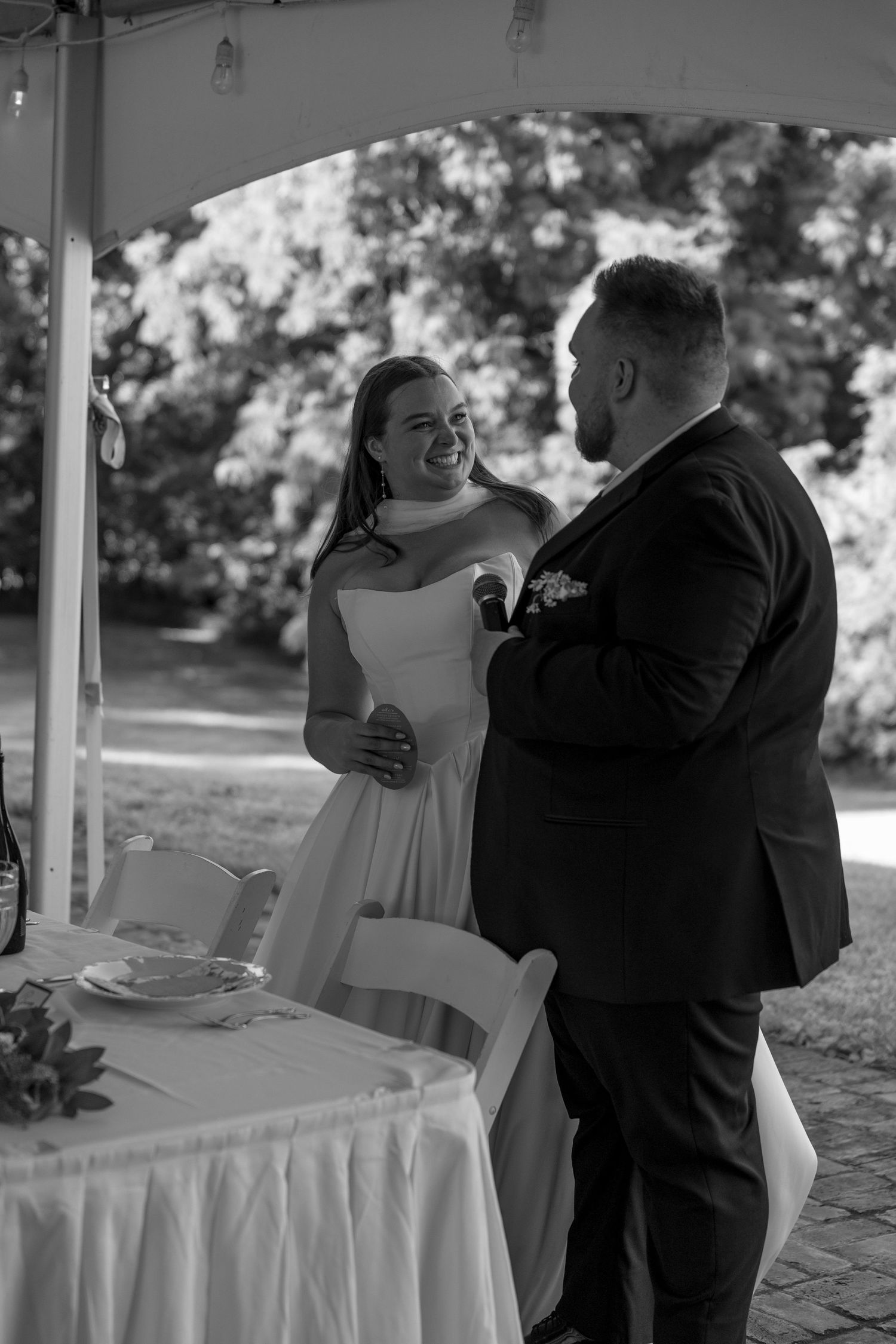 Black and white photo of a couple dancing during a reception under a covered outdoor venue.