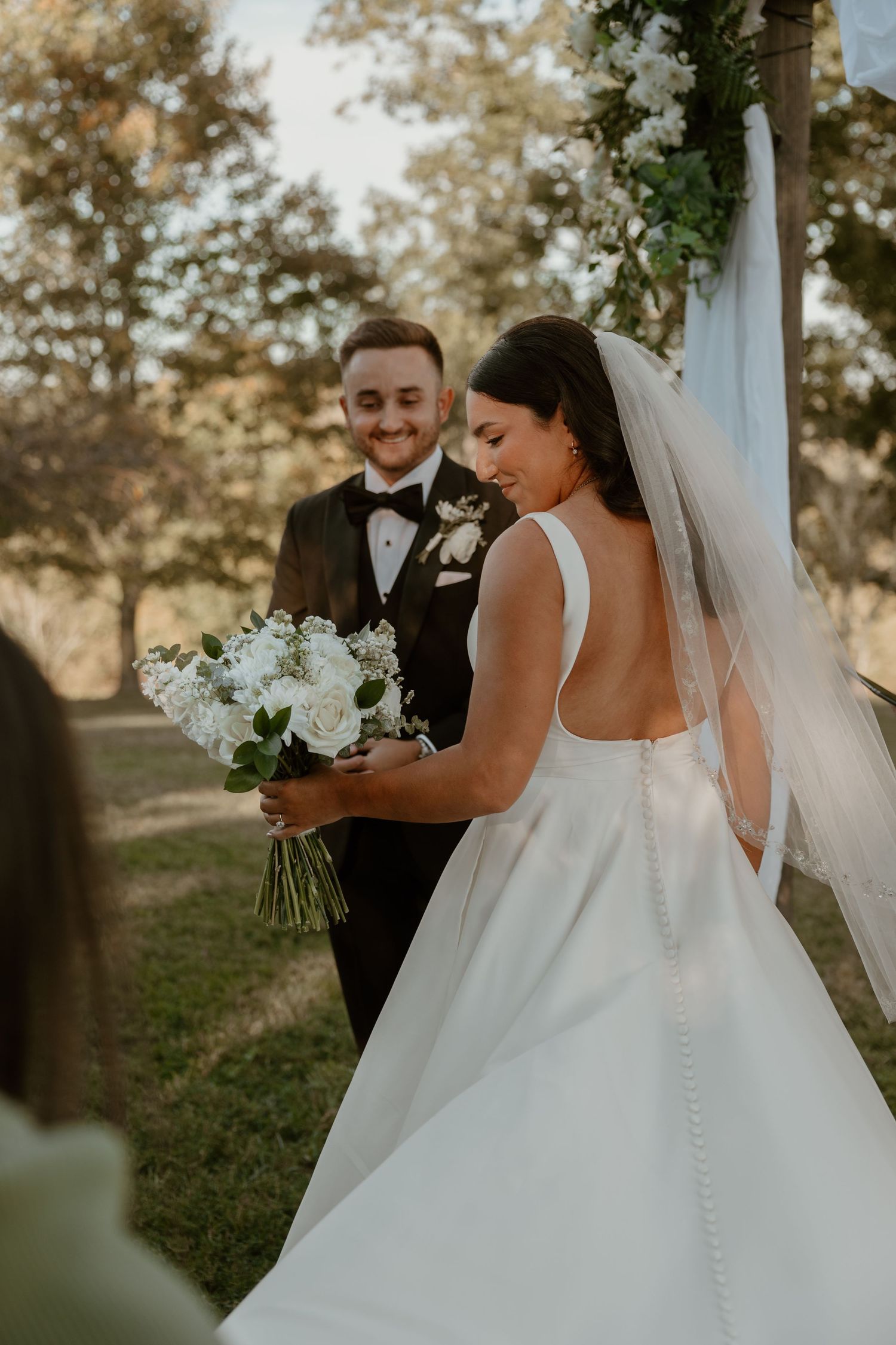 A couple shares a special moment during their outdoor wedding ceremony under floral decorations.