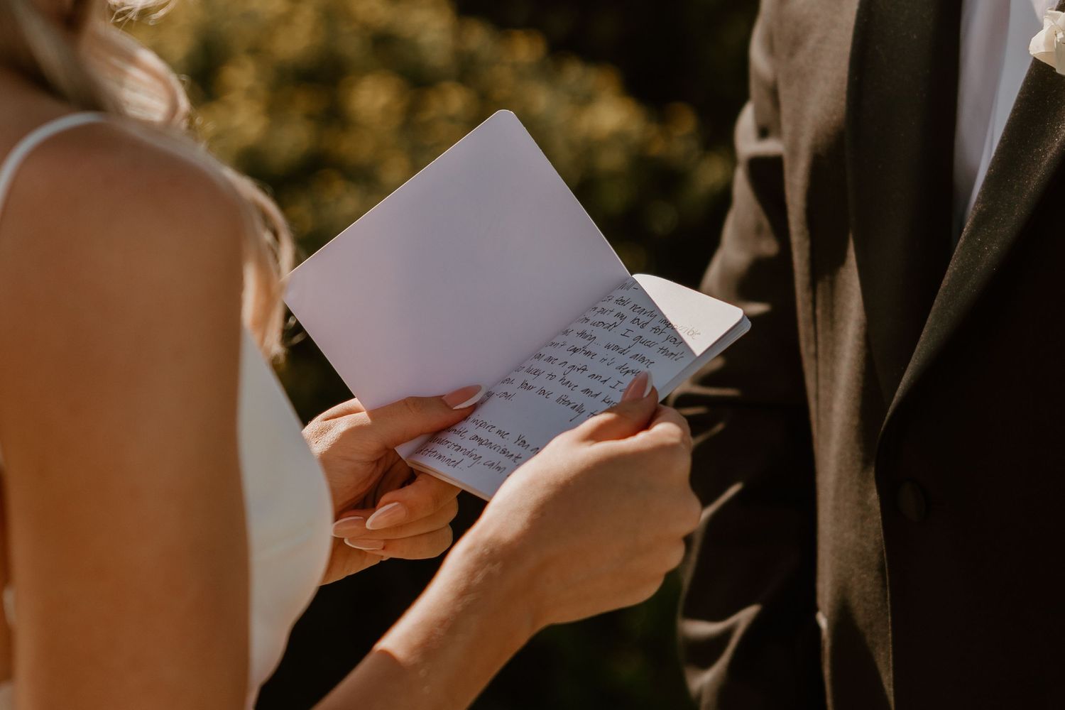 Close-up shot of hands holding wedding vow papers during an outdoor ceremony.
