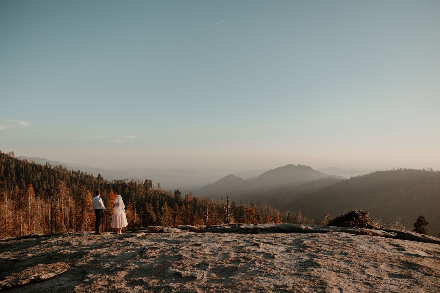 Sweeping mountain vista with golden sunset light illuminating couple in foreground.