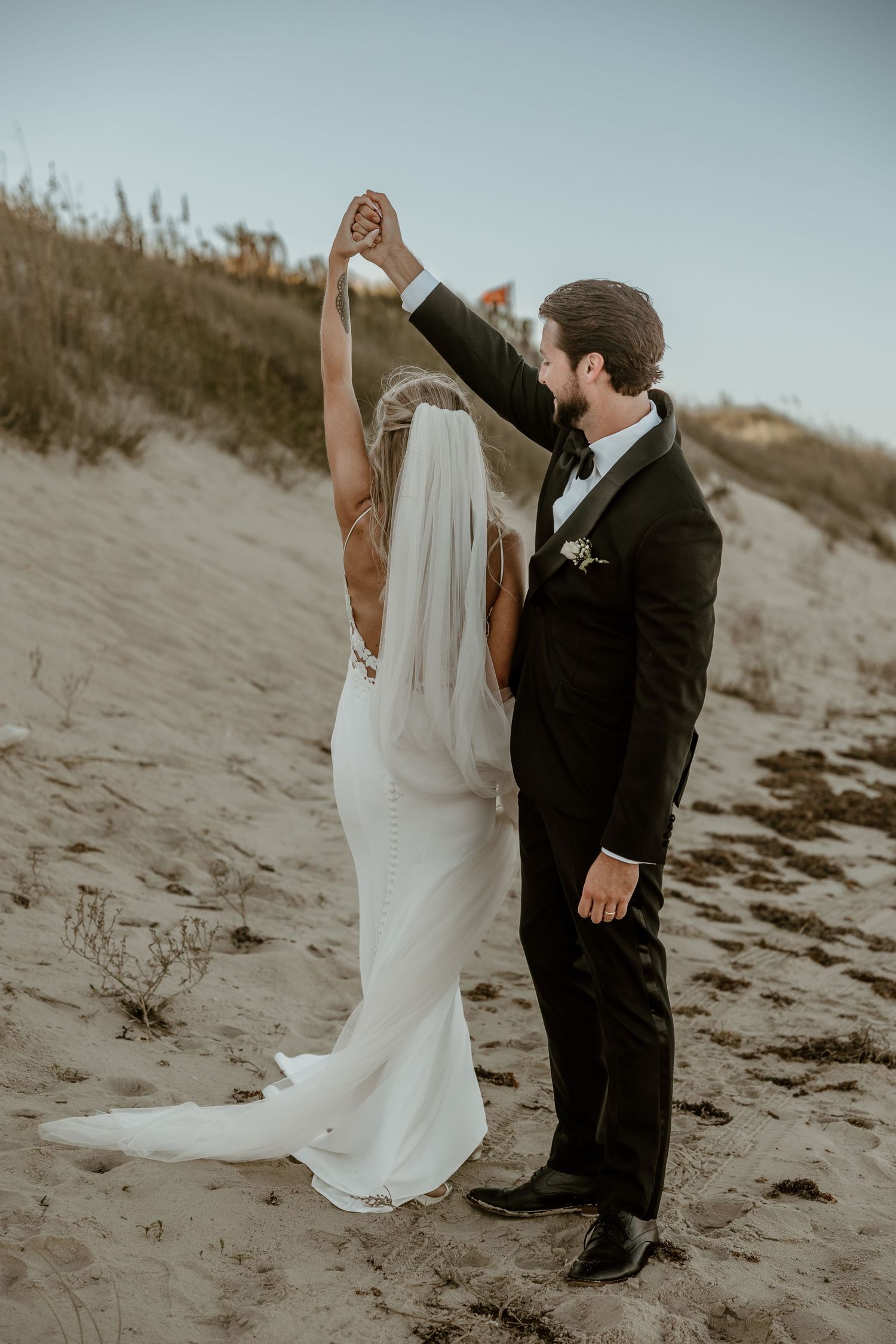 A couple shares a romantic dance moment on a sandy beach with dunes in the background.
